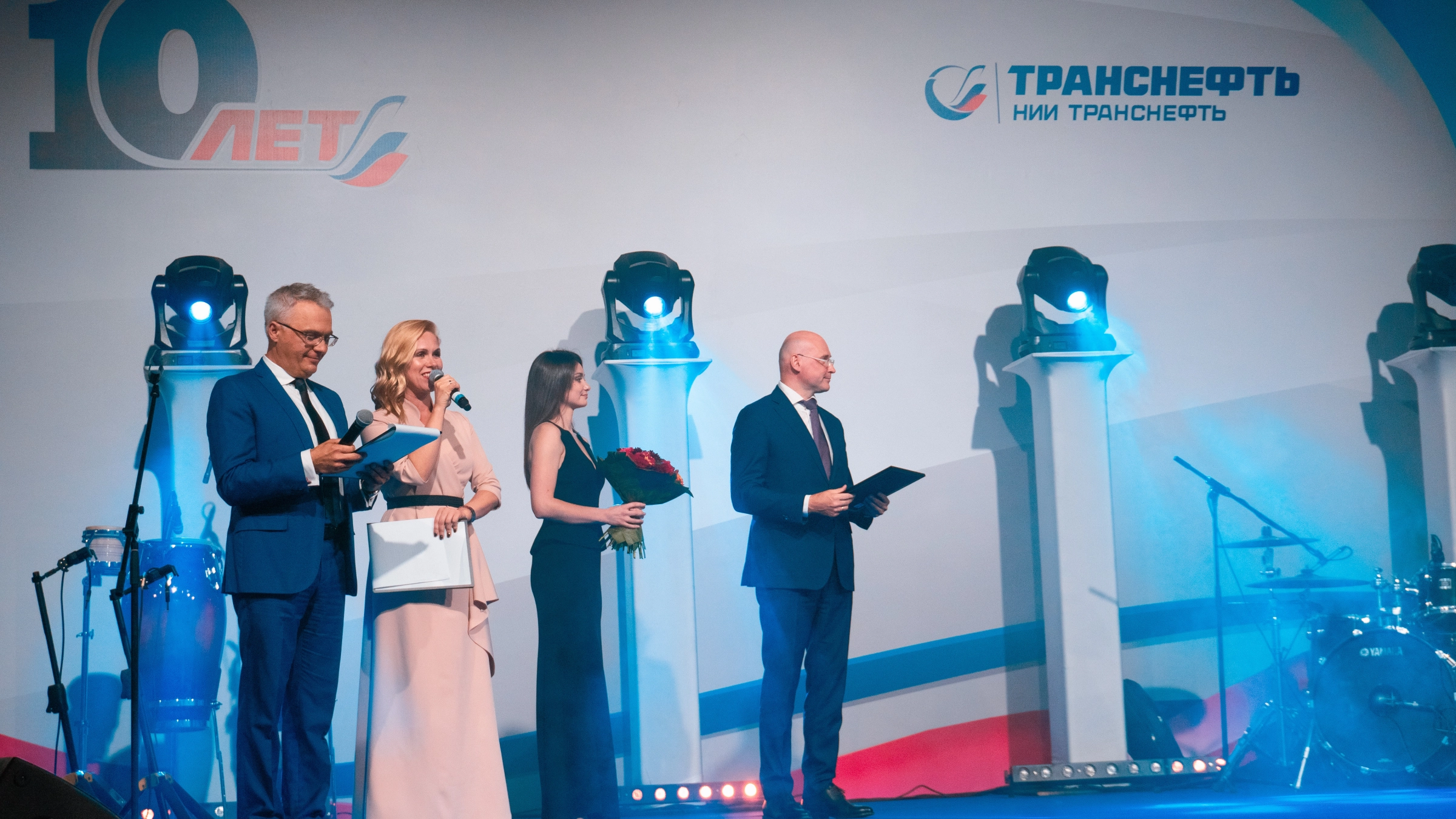 ведущие на сцене корпоративного мероприятия с логотипом компании