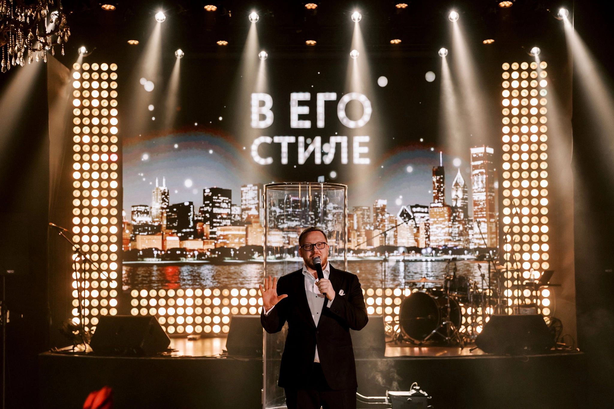 ведущий с микрофоном выступает на фоне экрана ночного города