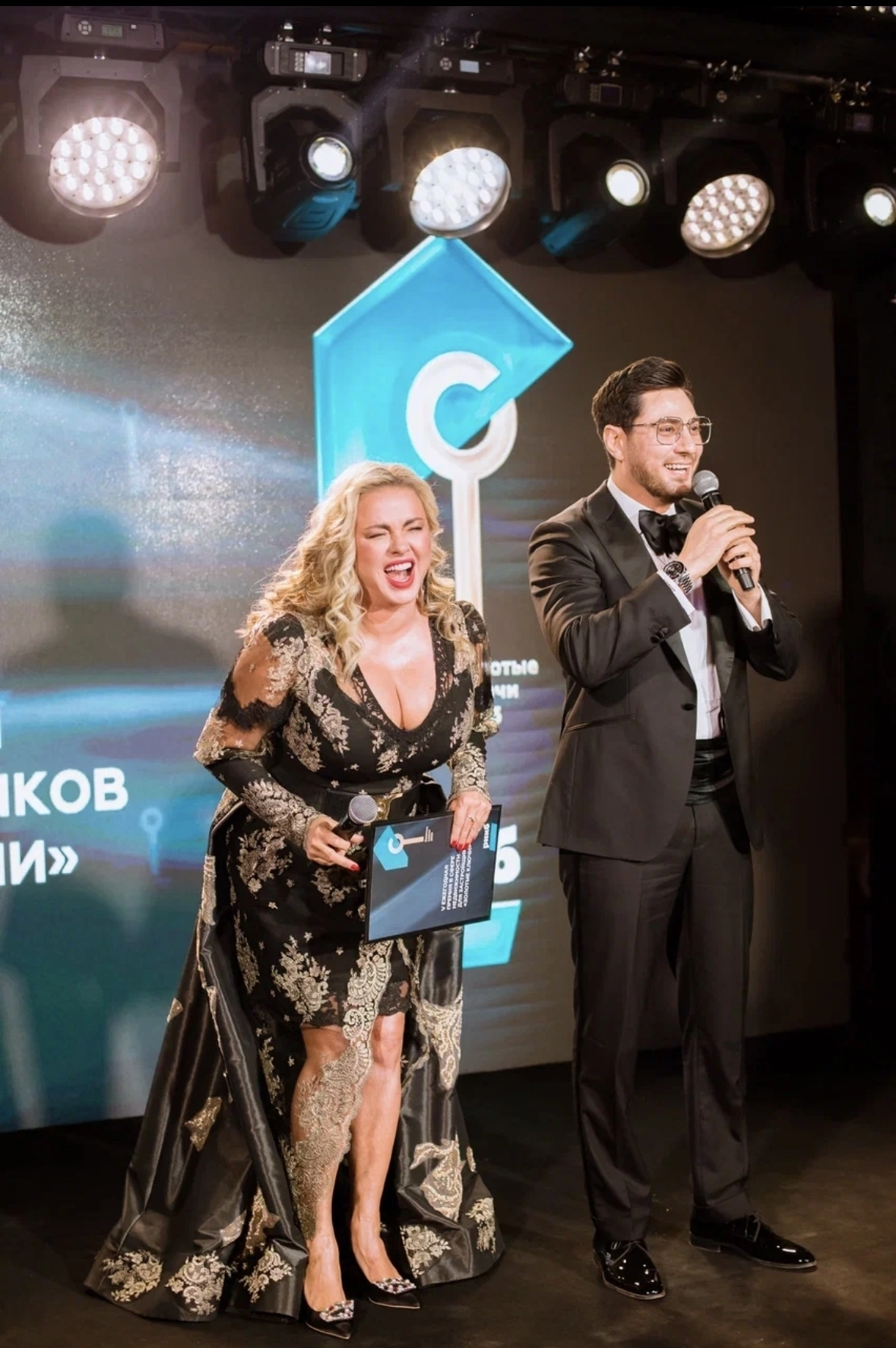ведущий и женщина в платье с наградой на сцене премии