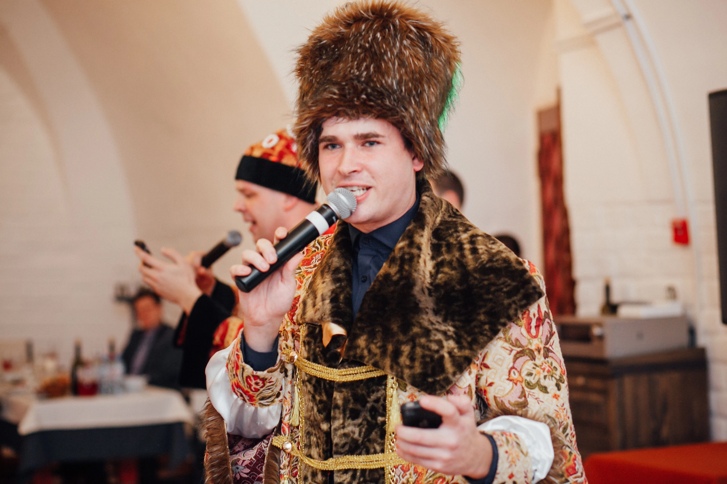 Мужчина в меховой шапке и кафтане поёт с микрофоном на празднике