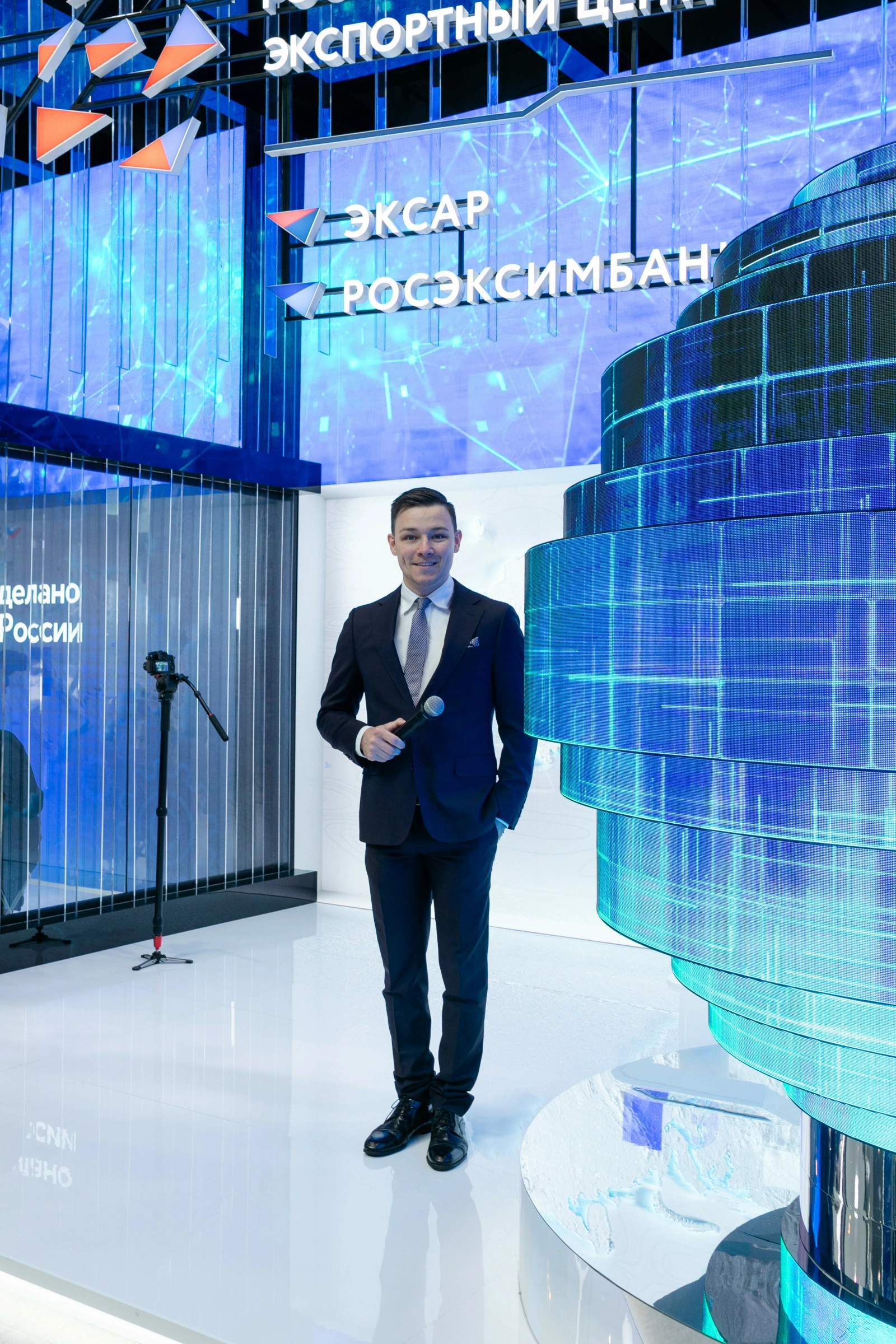 ведущий с микрофоном у стенда экспортного центра на выставке