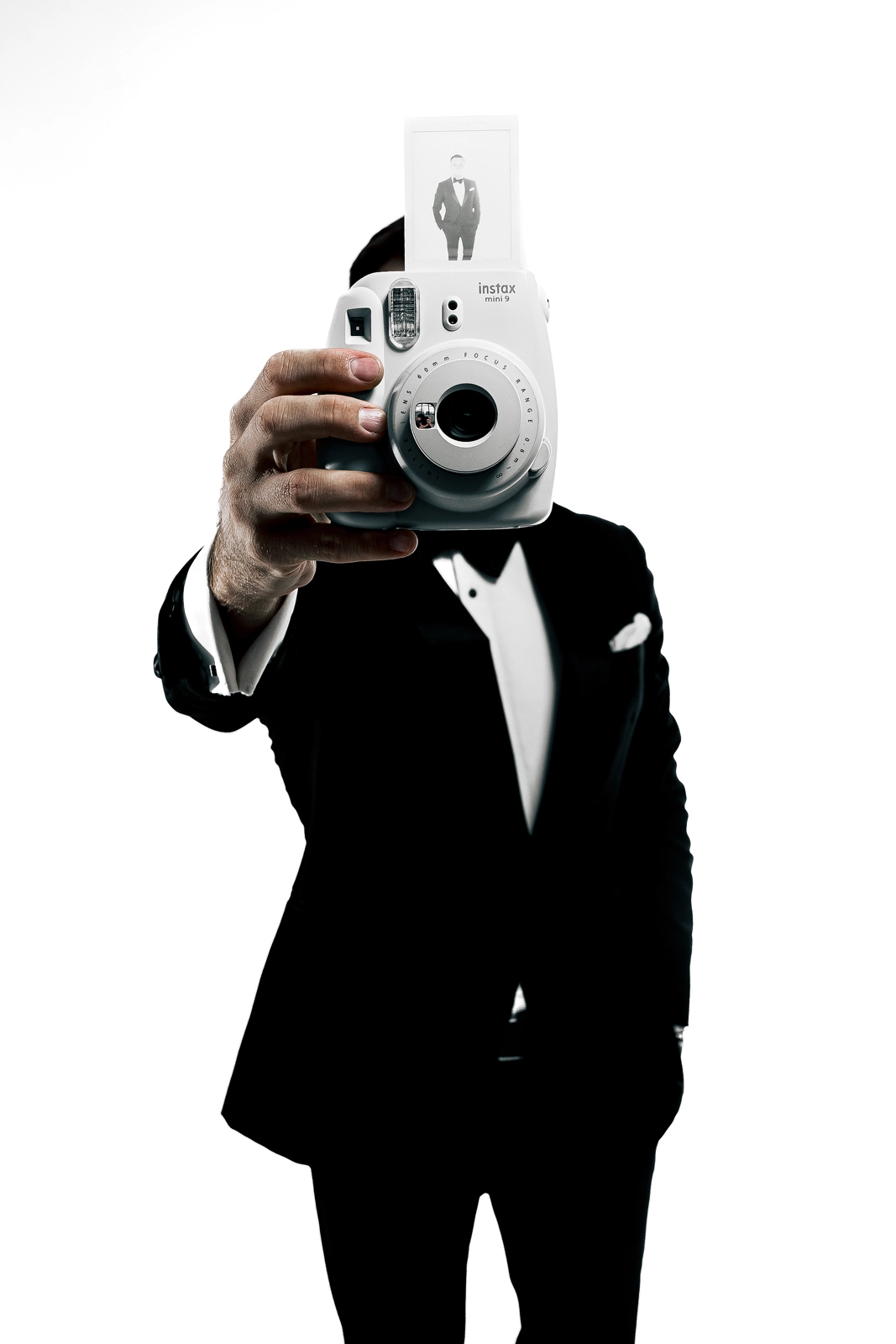 ведущий в чёрном смокинге с фотоаппаратом instax на белом фоне
