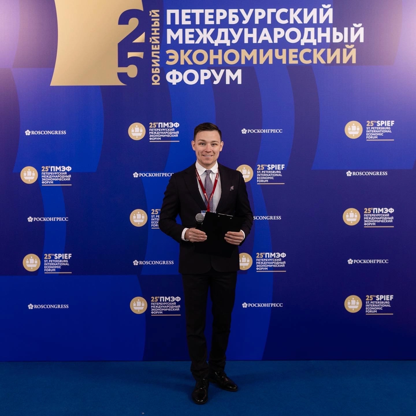 ведущий с микрофоном на фоне стенда делового форума