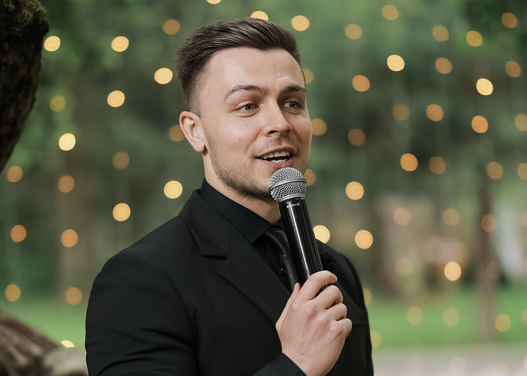 Ведущий с микрофоном на фоне гирлянды вечером на природе