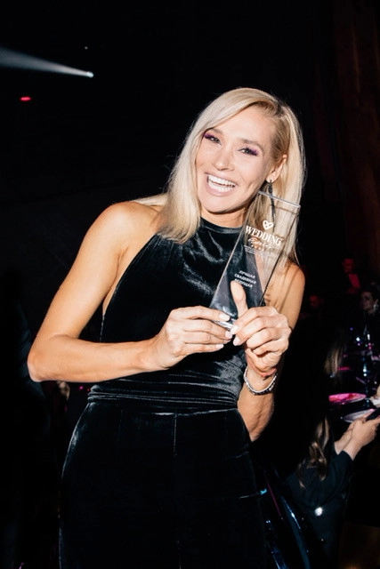 ведущая держит стеклянную статуэтку премии Wedding Awards на сцене