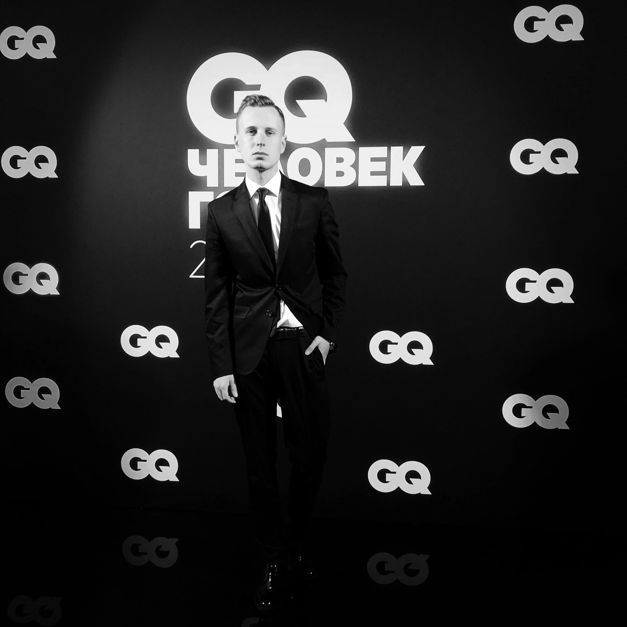 мужчина в чёрном костюме на фоне пресс-волла премии GQ