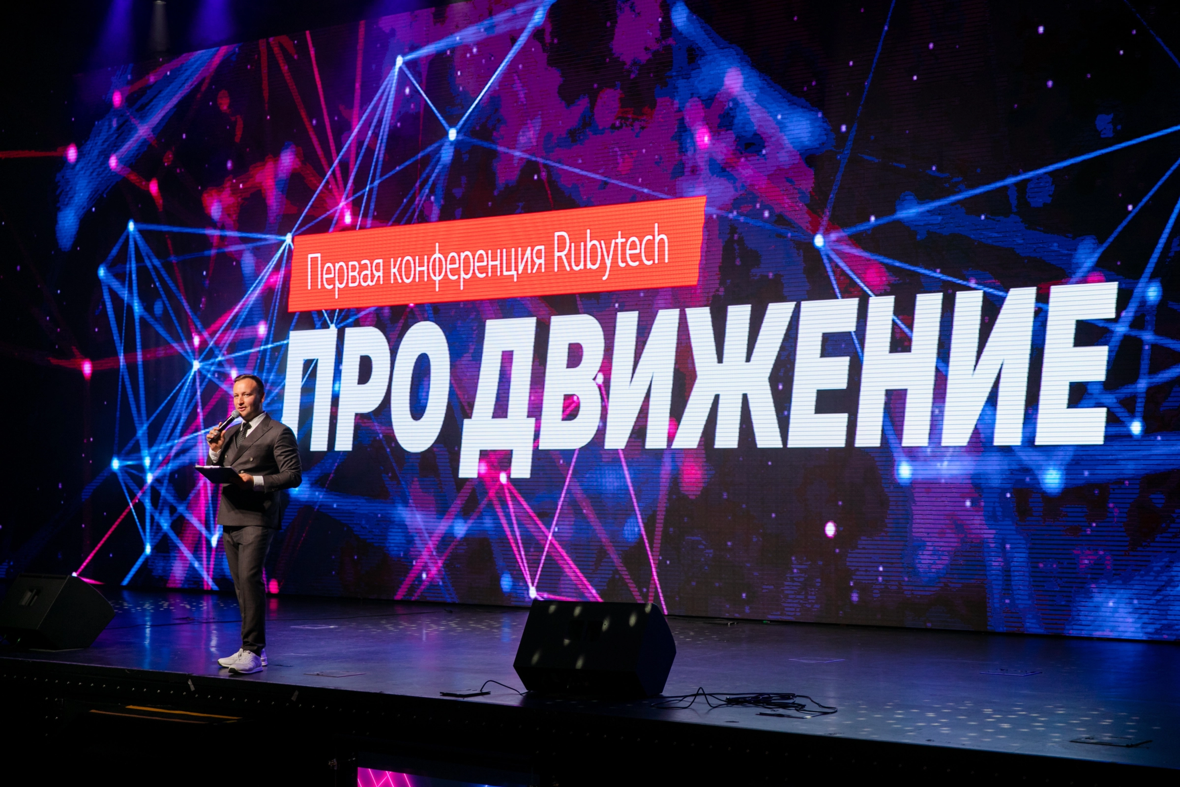 ведущий с микрофоном выступает на фоне яркого led-экрана конференции