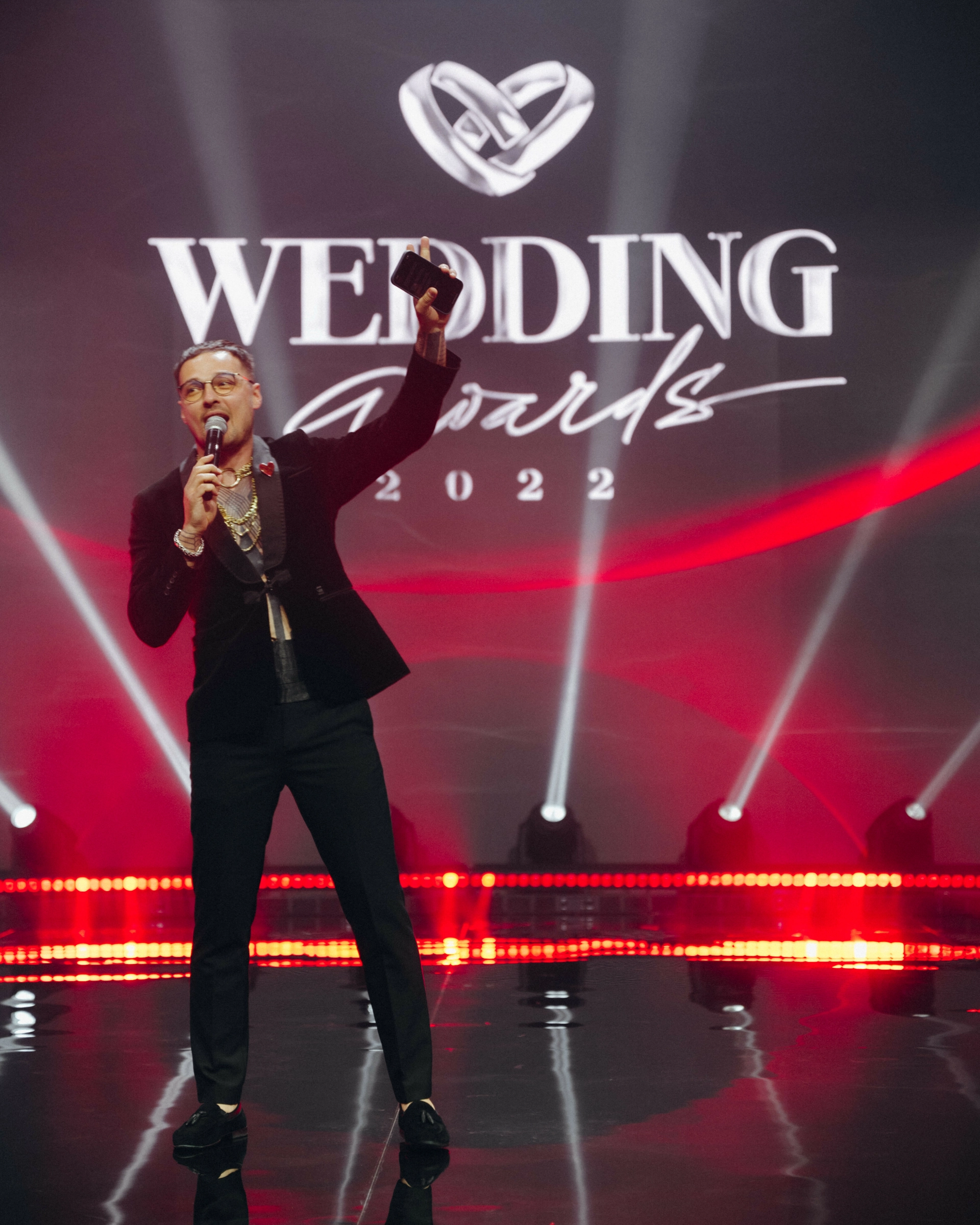 Ведущий с поднятой рукой и микрофоном на сцене Wedding Awards