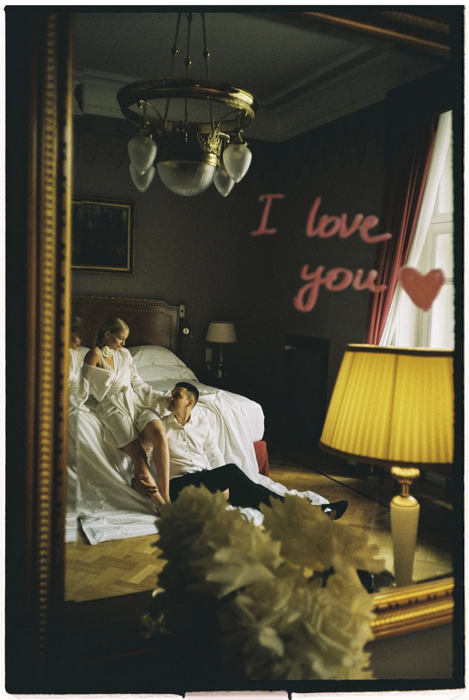 Отражение жениха и невесты в зеркале с надписью I love you в номере отеля