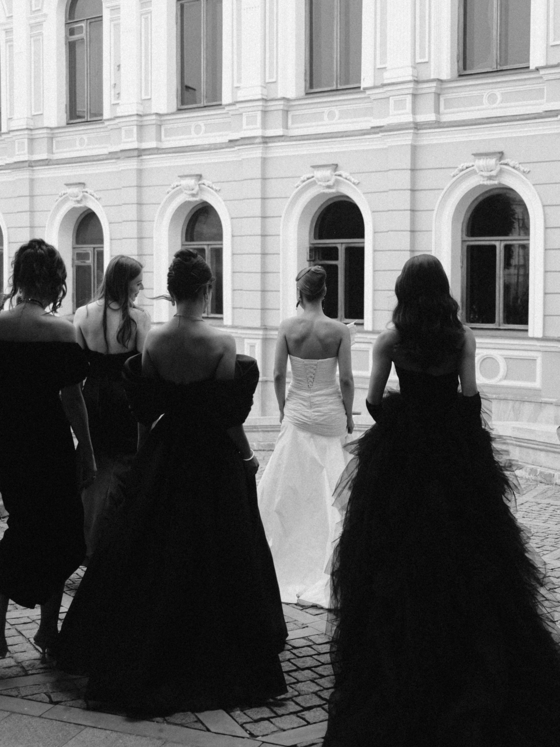 Невеста в белом платье со спины среди подружек в чёрных платьях
