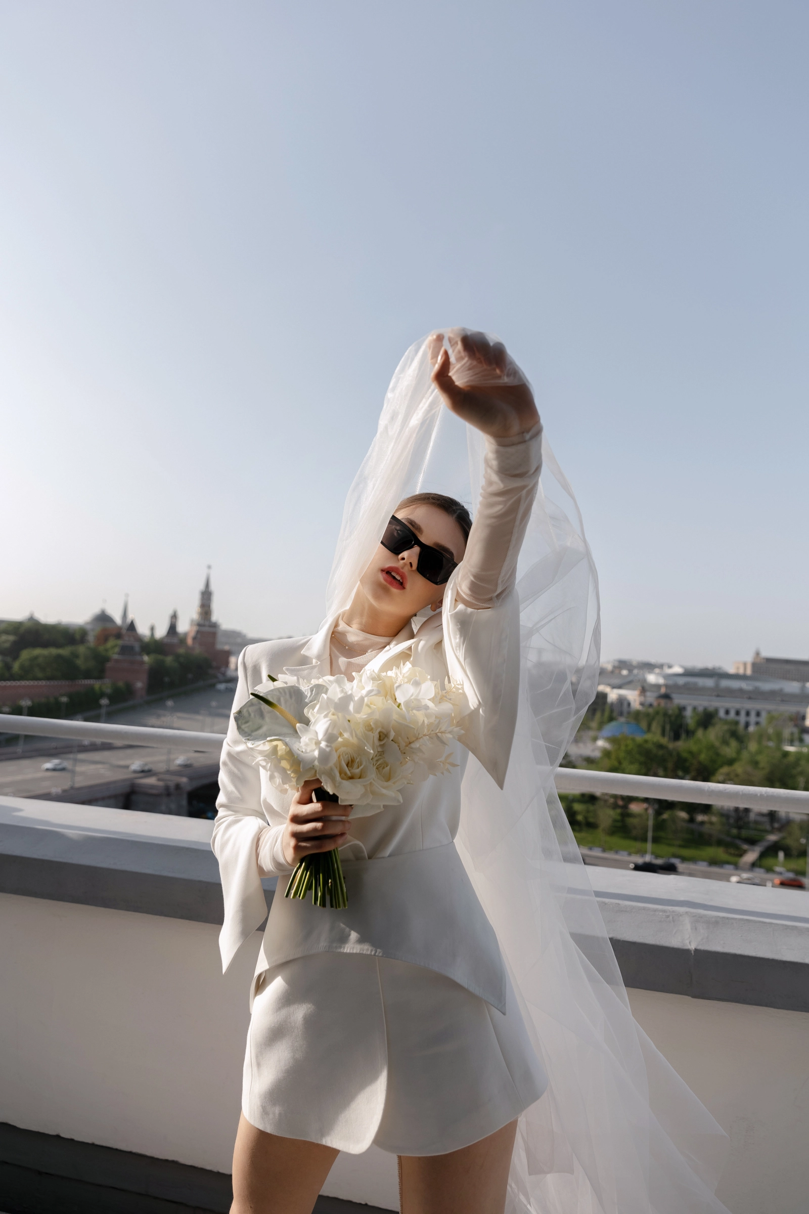 невеста в белом костюме с поднятой фатой на фоне исторического центра города