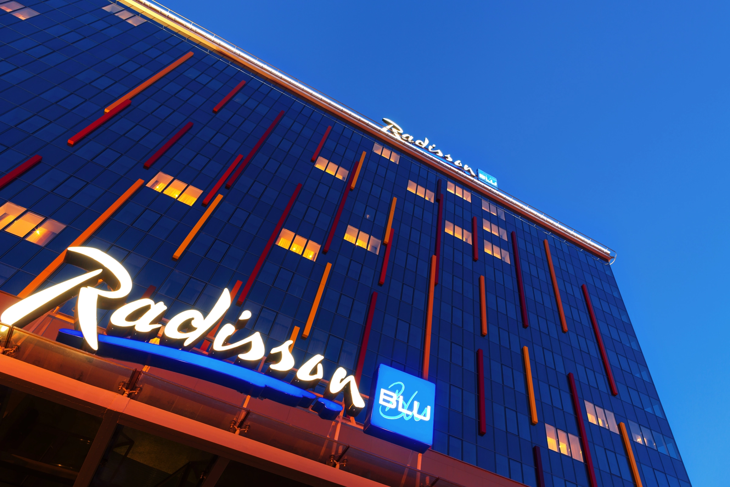 Фасад отеля Radisson Blu в сумерках с красно-оранжевой подсветкой здания