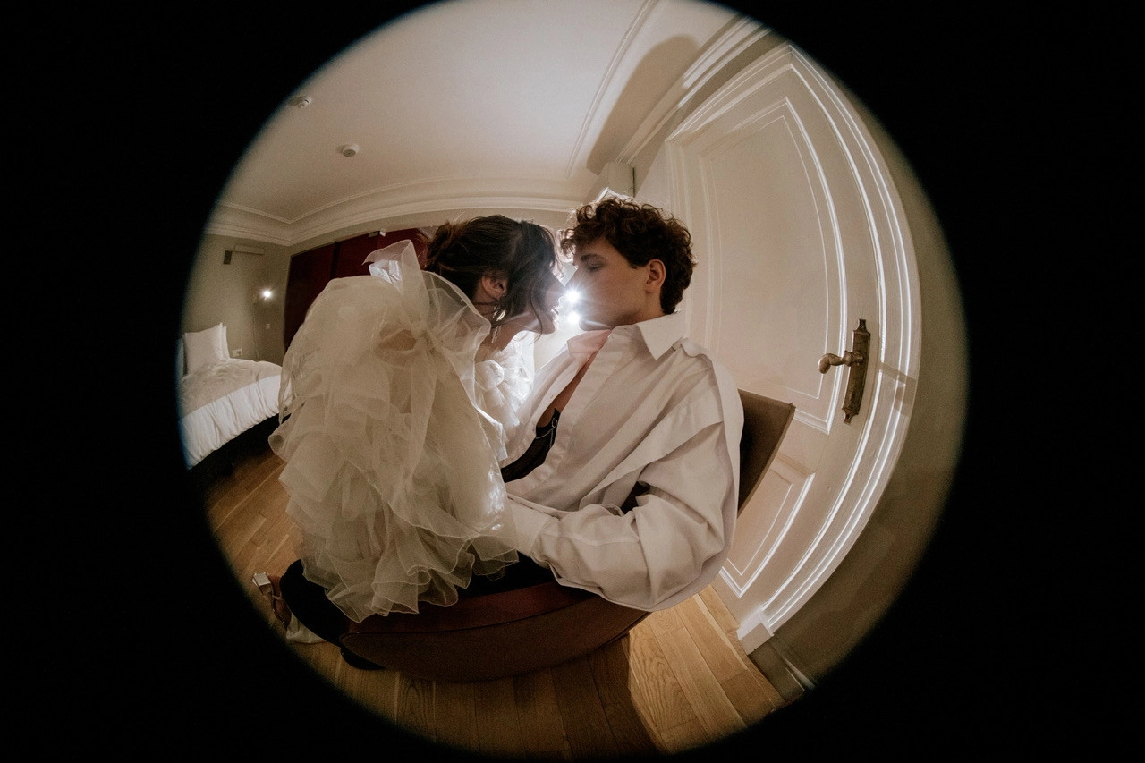 Жених и невеста лбами друг к другу в номере отеля, кадр через fisheye-объектив