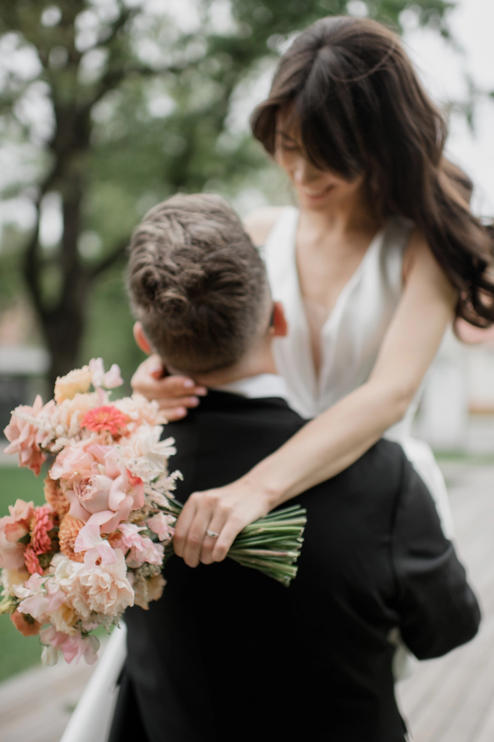 невеста обнимает жениха с букетом розовых и персиковых цветов на улице