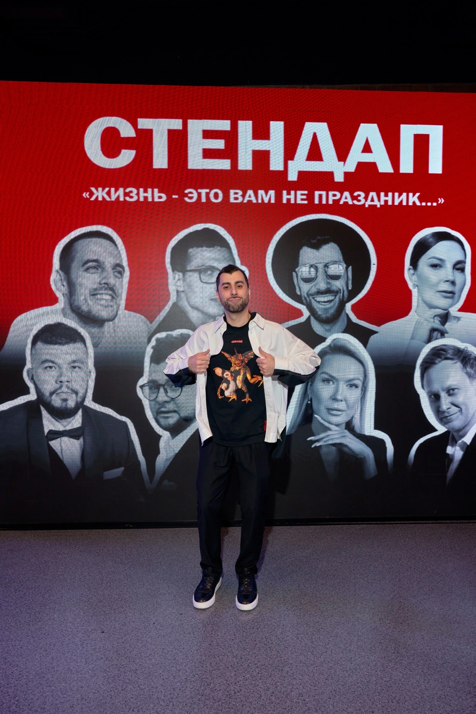 ведущий показывает жест одобрения на фоне афиши стендап-шоу