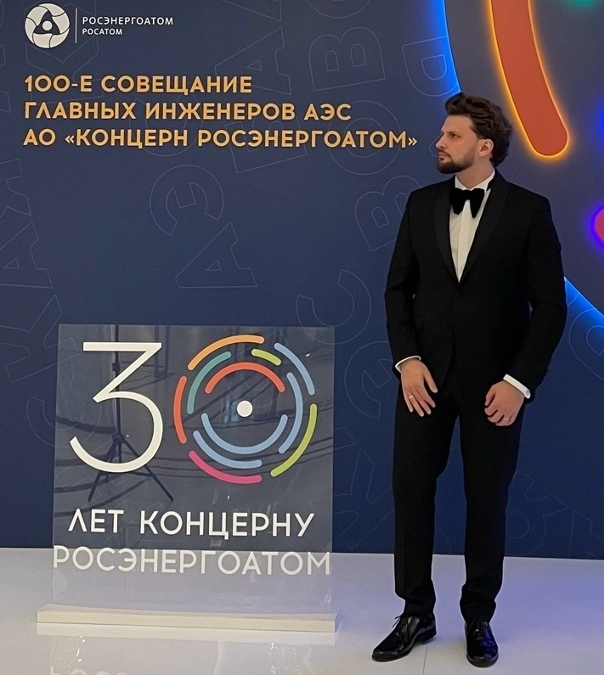 мужчина в смокинге с бабочкой на фоне корпоративного стенда с подсветкой