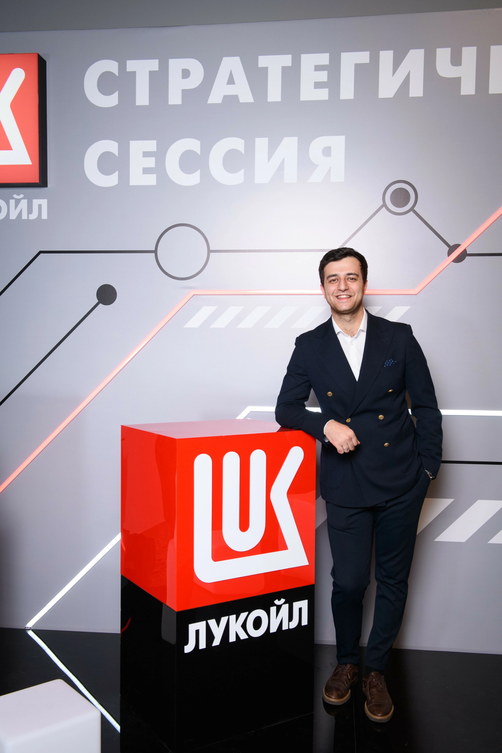 ведущий в костюме улыбается у брендированного стенда делового мероприятия