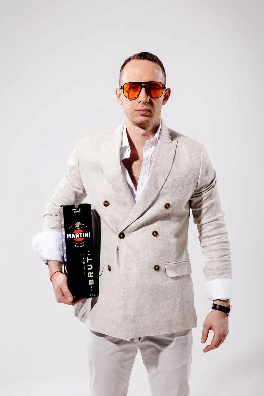 мужчина в бежевом костюме с коробкой Martini Brut на белом фоне