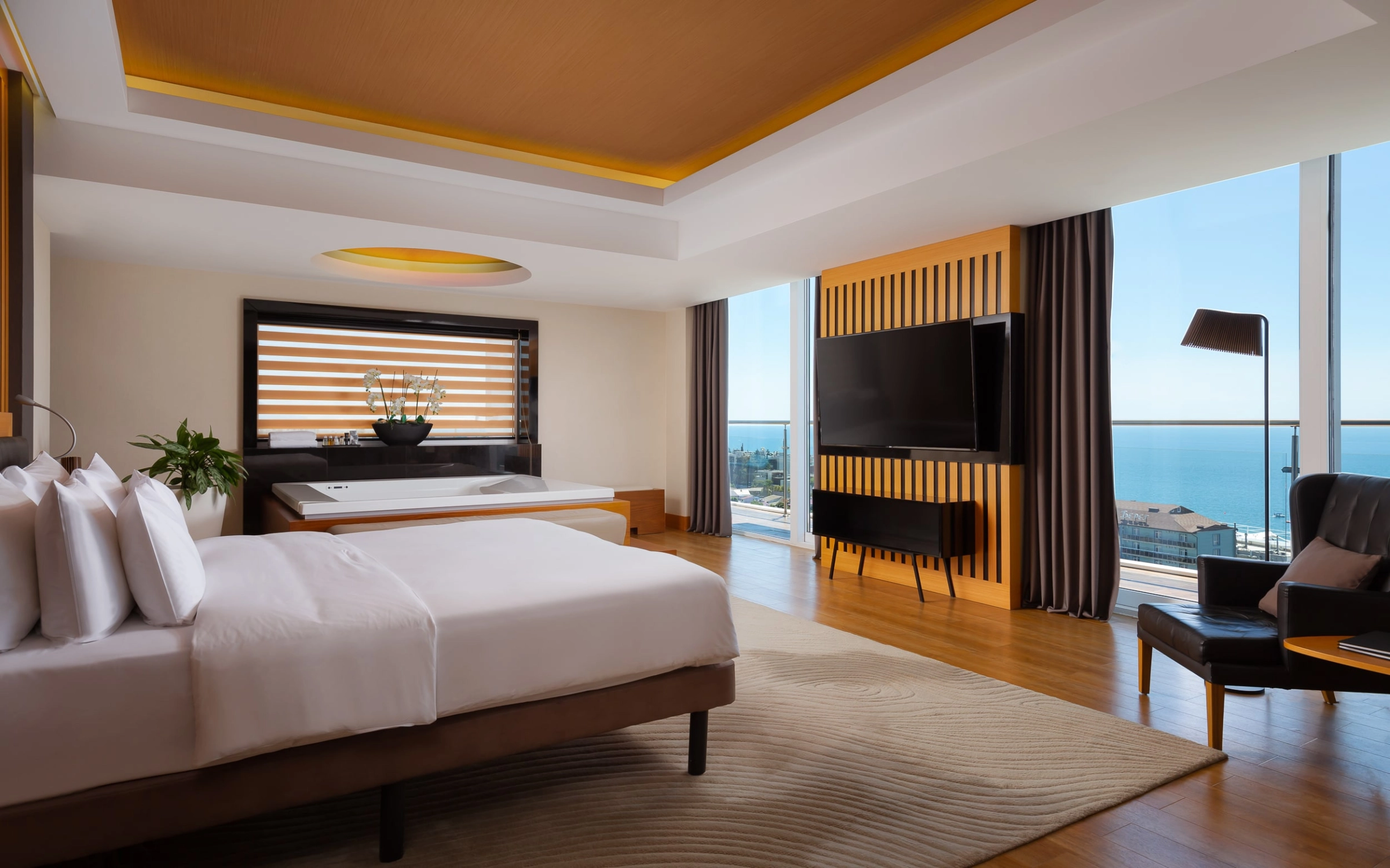 Modern suite bedroom with white bedding and golden ceiling accent overlooking sea