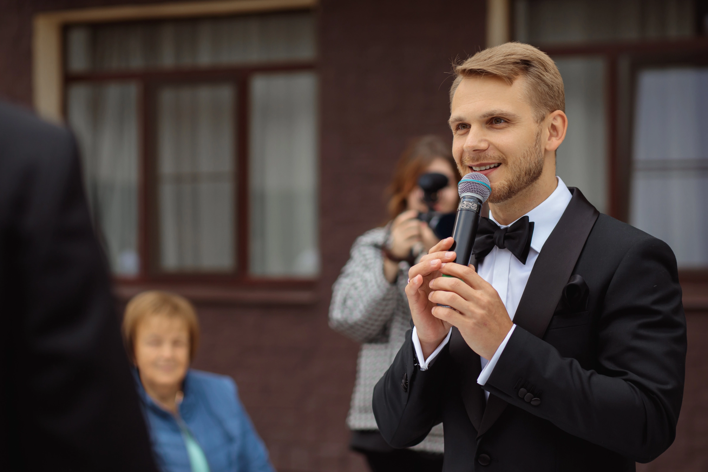 ведущий в шляпе говорит в микрофон держа планшет