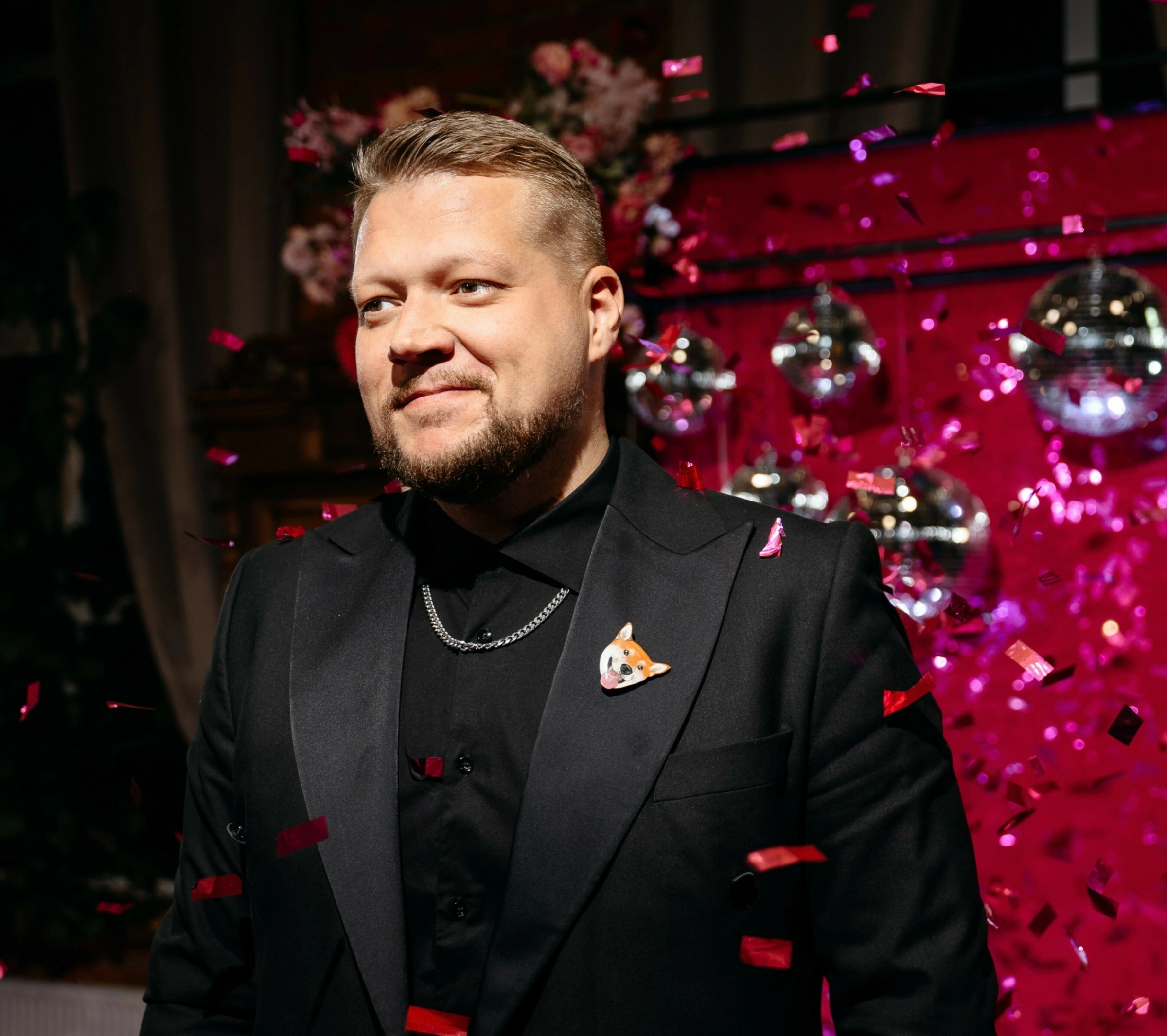 Ведущий свадьбы улыбается на фоне дискошаров и красного конфетти вечеринки