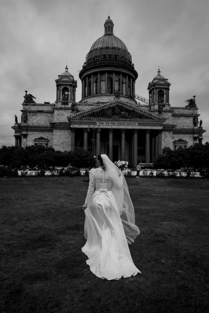 невеста в кружевном платье со шлейфом на фоне купола собора чёрно-белом кадре