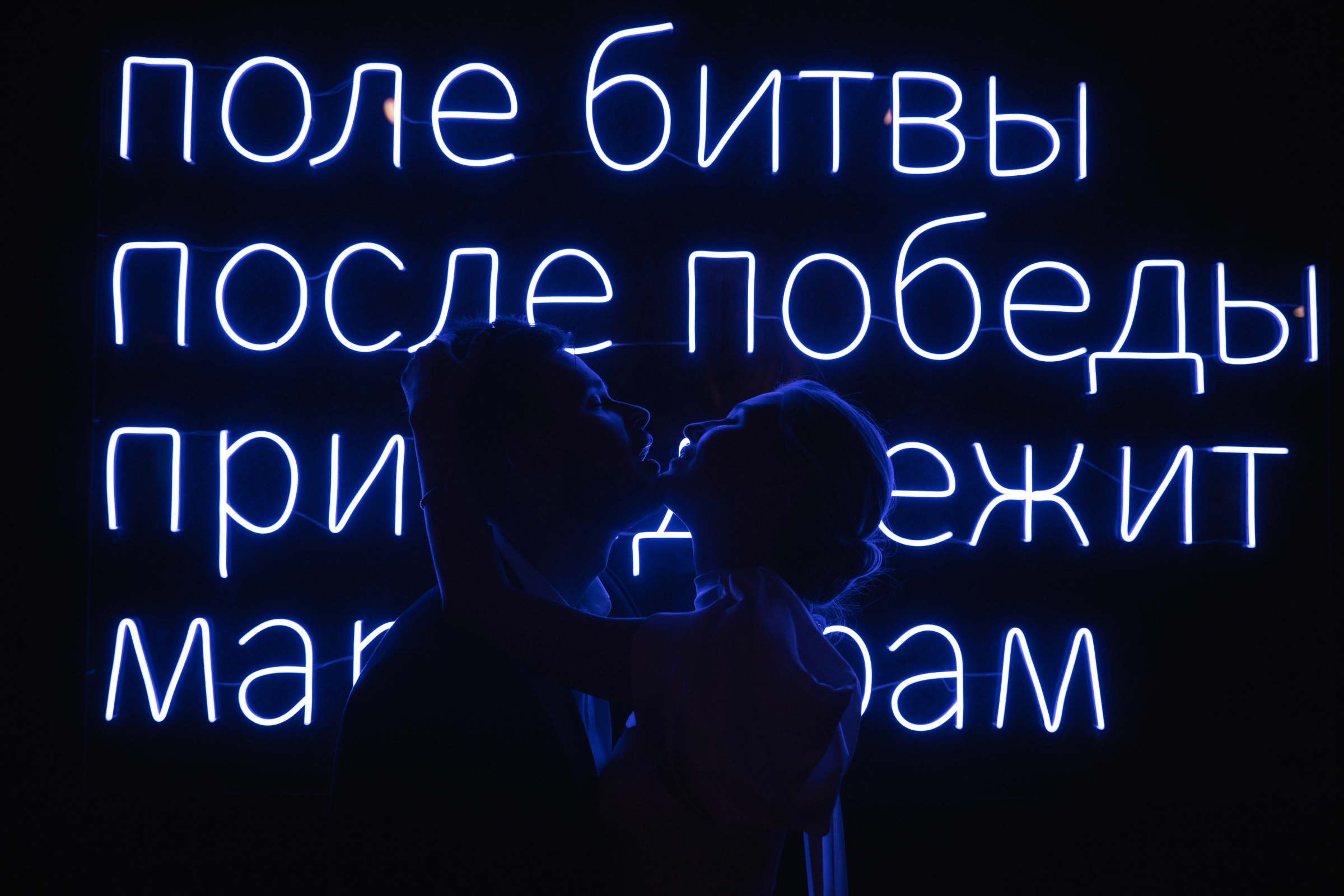 силуэты жениха и невесты целуются на фоне синей неоновой вывески