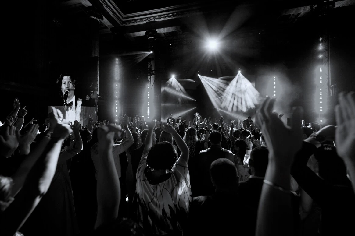 ведущий на сцене среди танцующих и поднимающих руки гостей вечера
