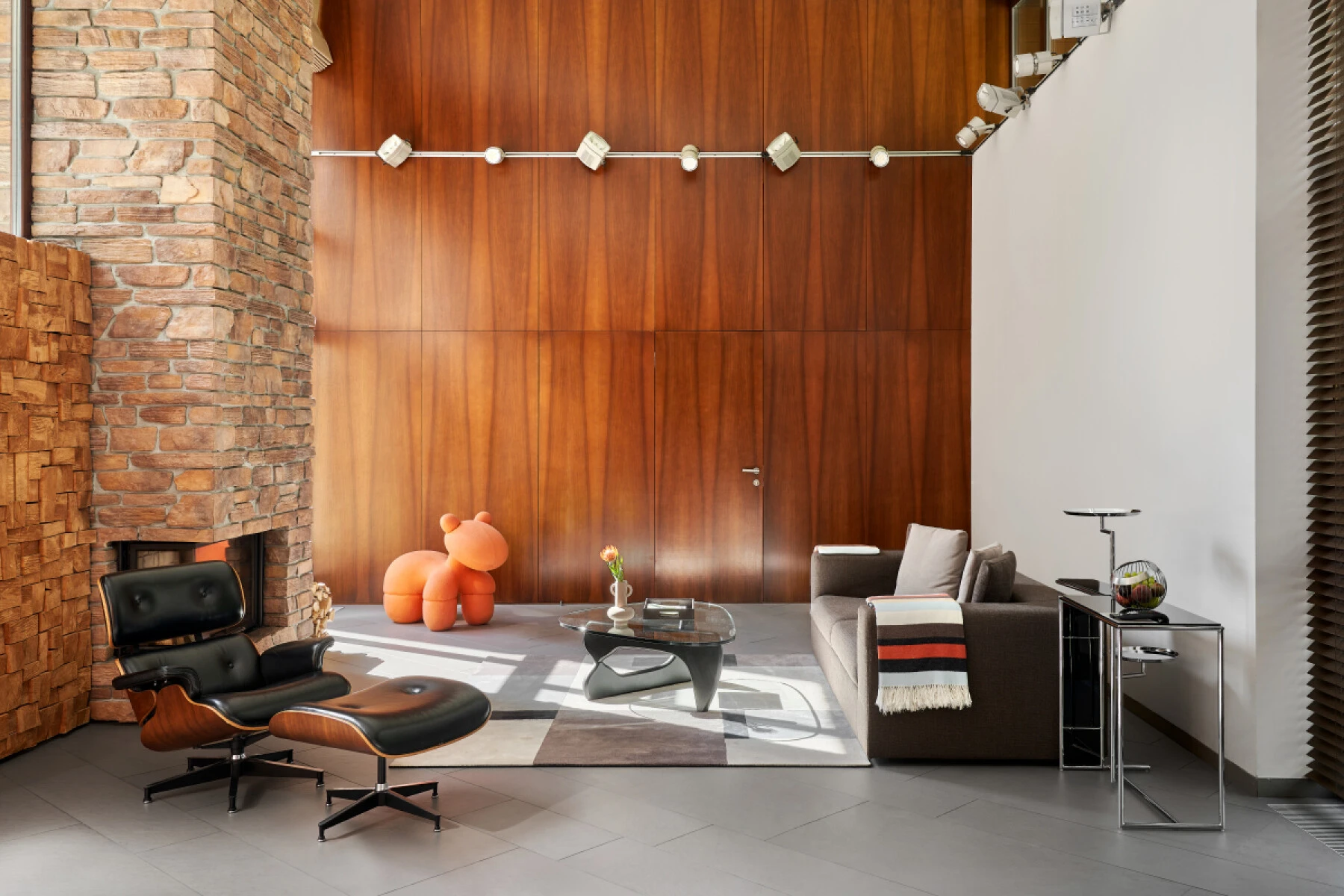 кресло Eames и диван в уютной гостиной с каменной стеной