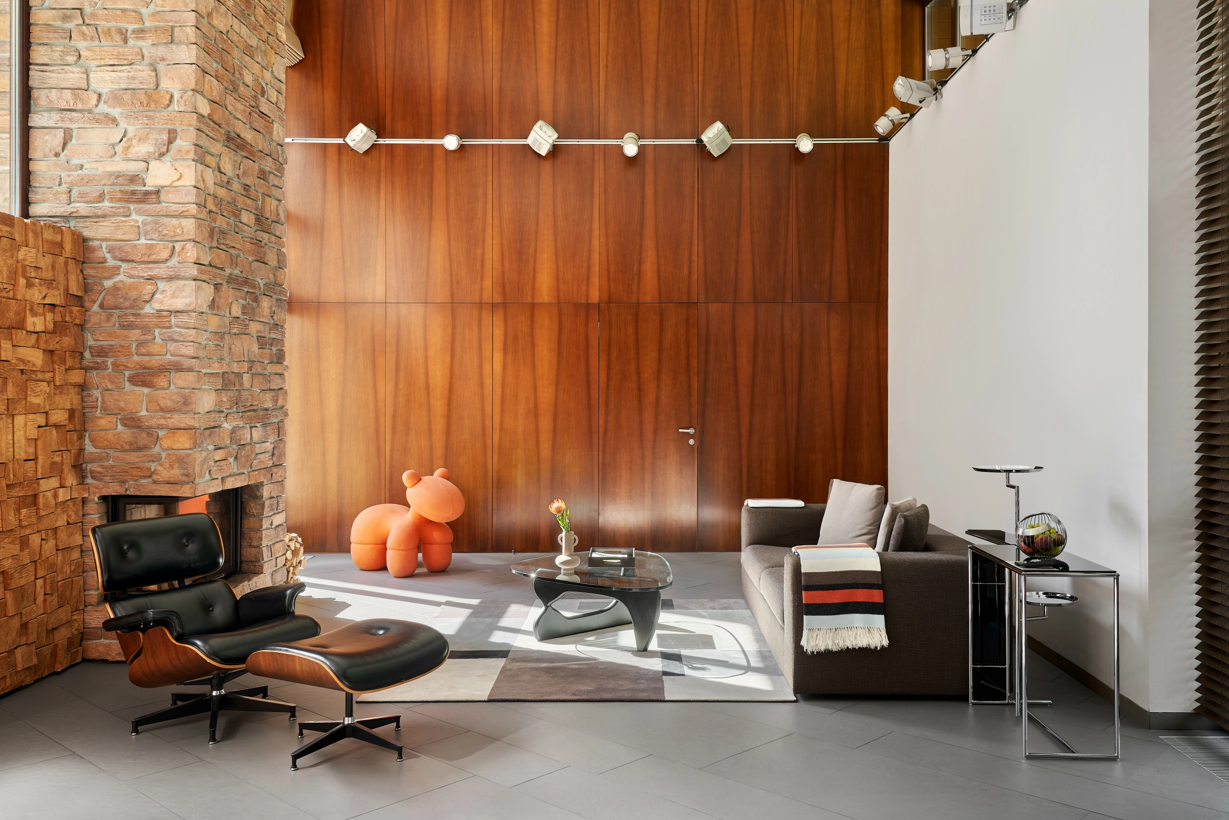 кресло Eames и диван в гостиной с каменной стеной и деревом