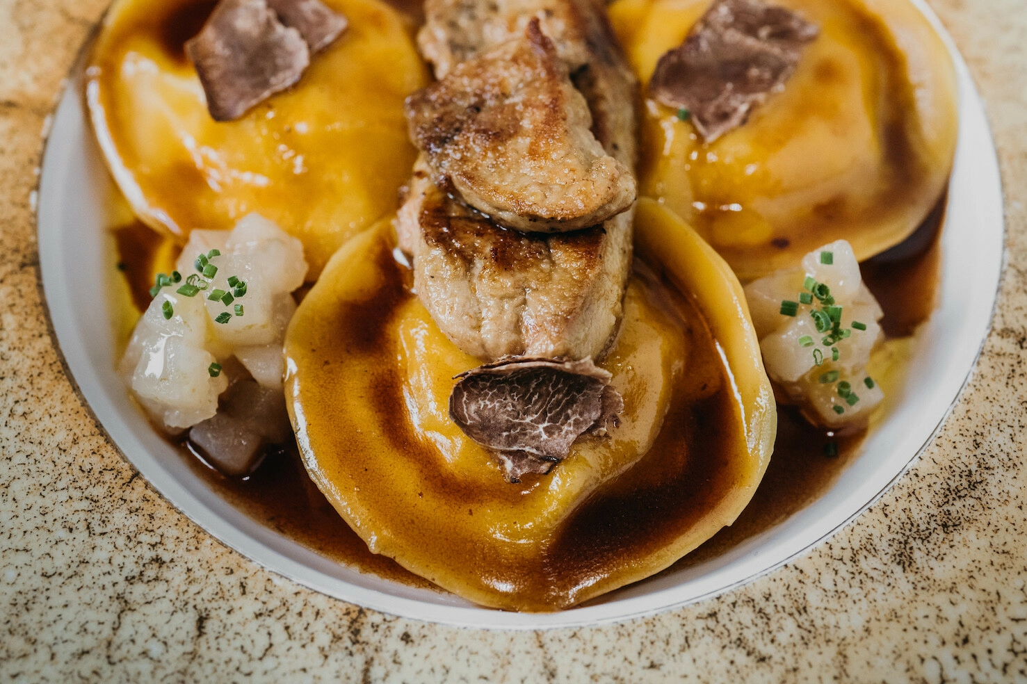равиоли с мясом, соусом и грушей на тарелке