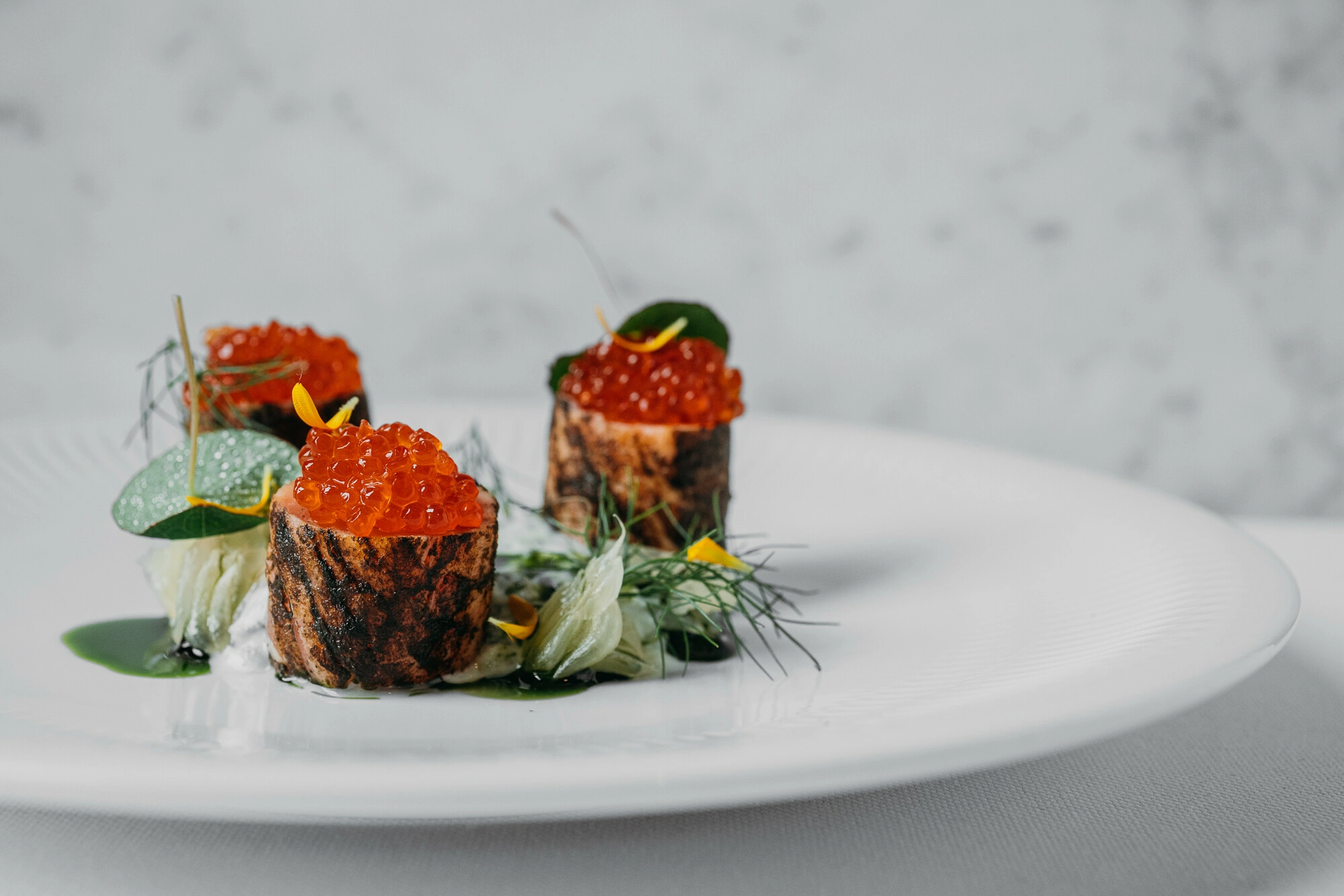 рулетики с красной икрой и зеленью на белой тарелке