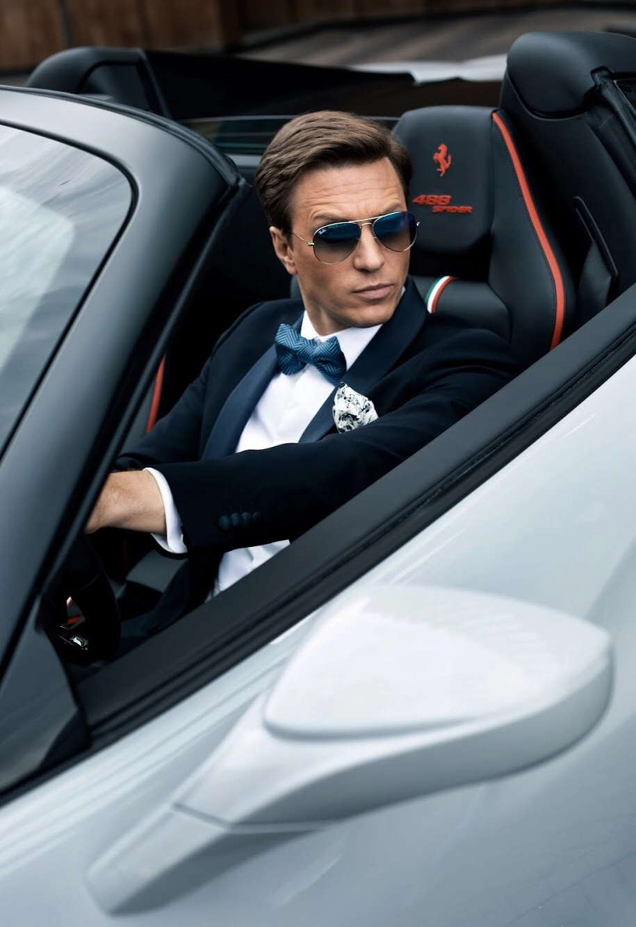 Мужчина в смокинге сидит за рулём белого кабриолета Ferrari