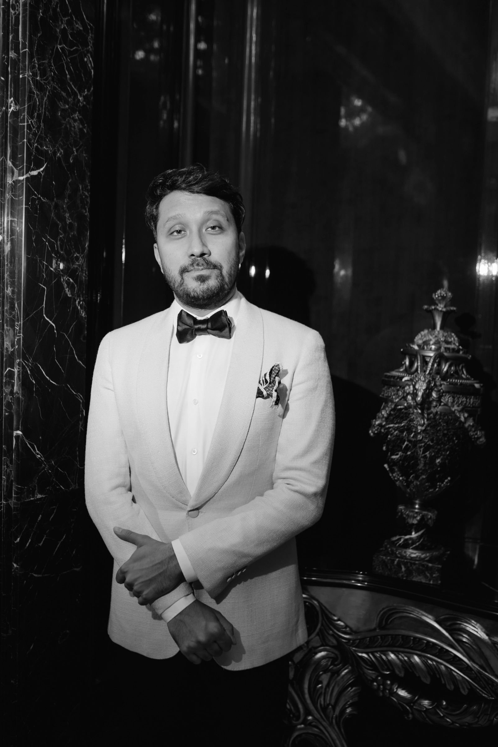 мужчина в кремовом смокинге с бабочкой на фоне мраморной стены
