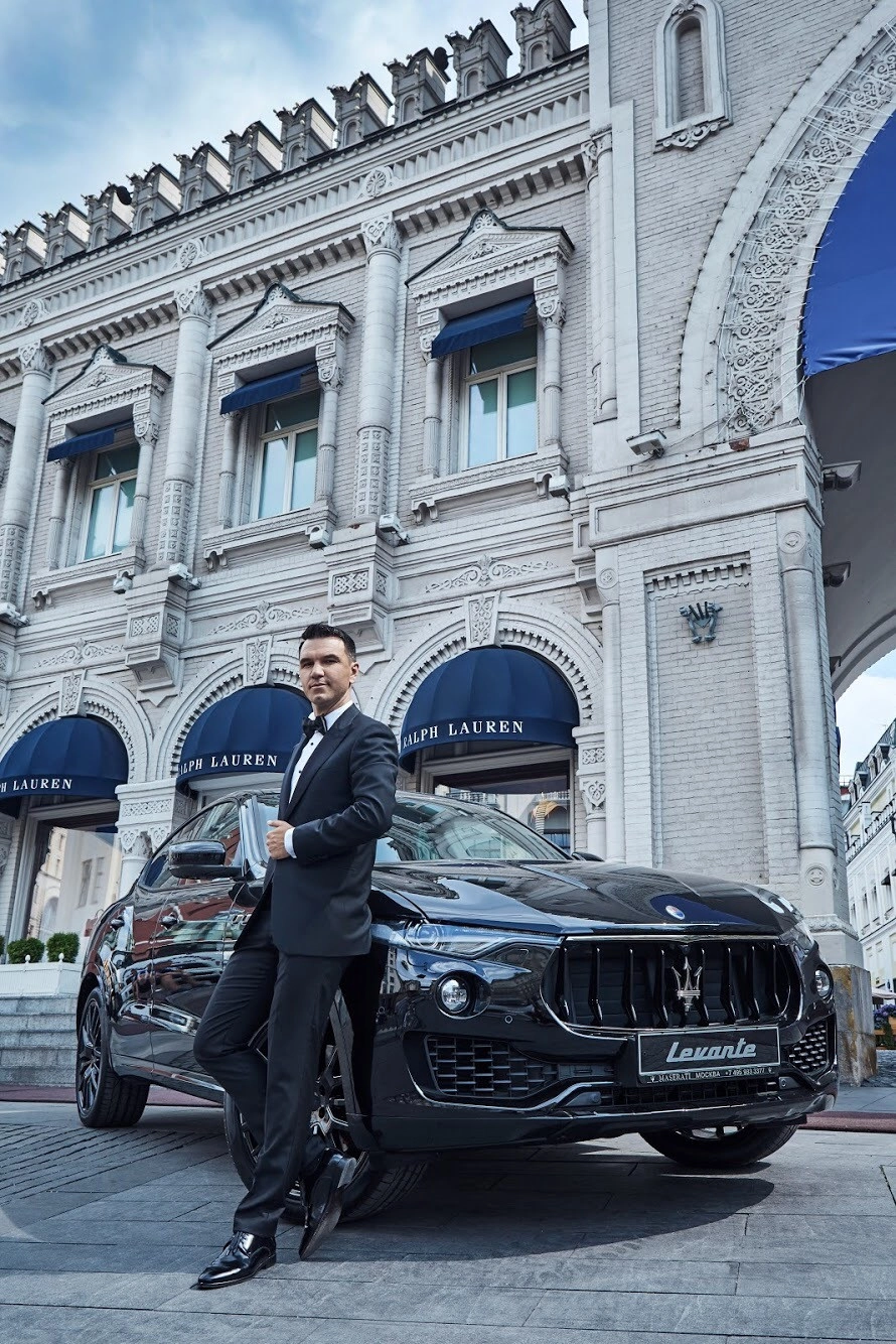 мужчина в смокинге стоит рядом с чёрным автомобилем Maserati
