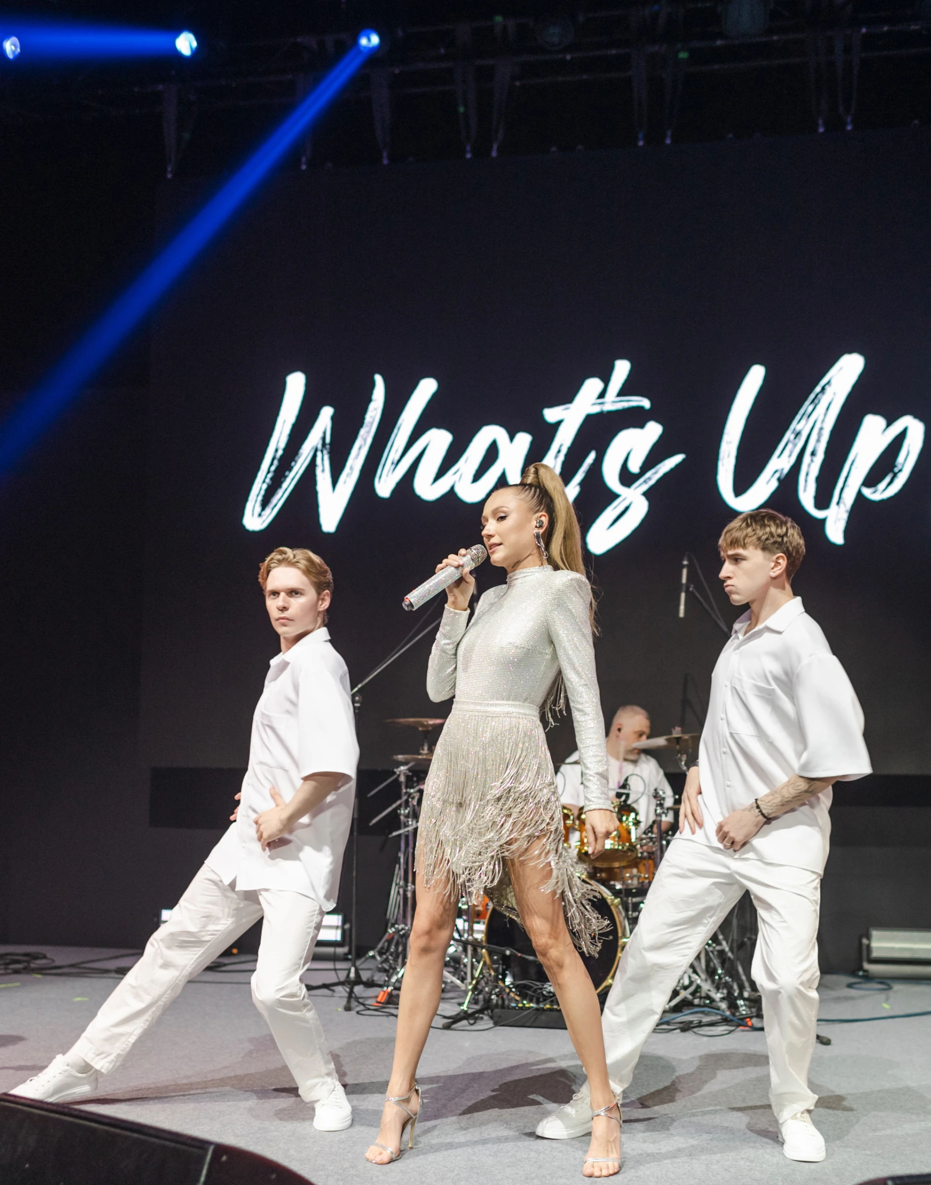 Солистка и танцоры WHAT'S UP выступают на сцене на фоне надписи WHAT'S UP
