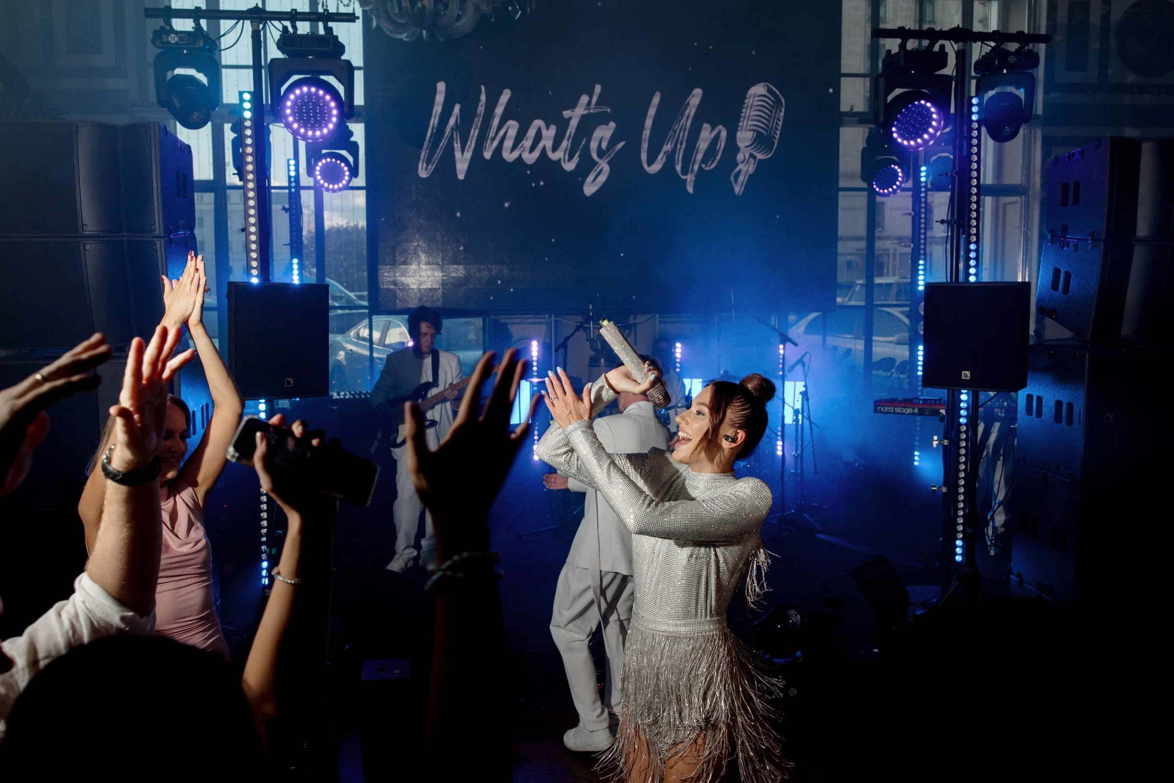 Певица WHAT'S UP поёт для гостей с поднятыми руками в синей подсветке сцены