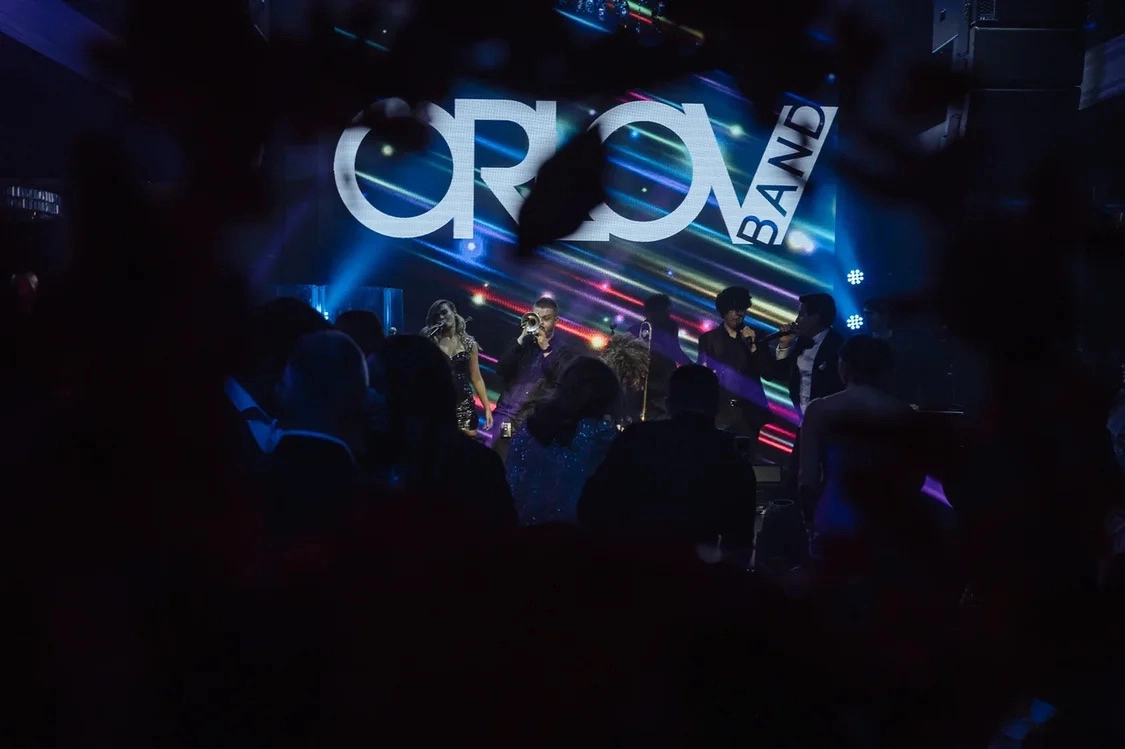 Музыканты выступают под неоновой вывеской Orlov Band на вечеринке для гостей