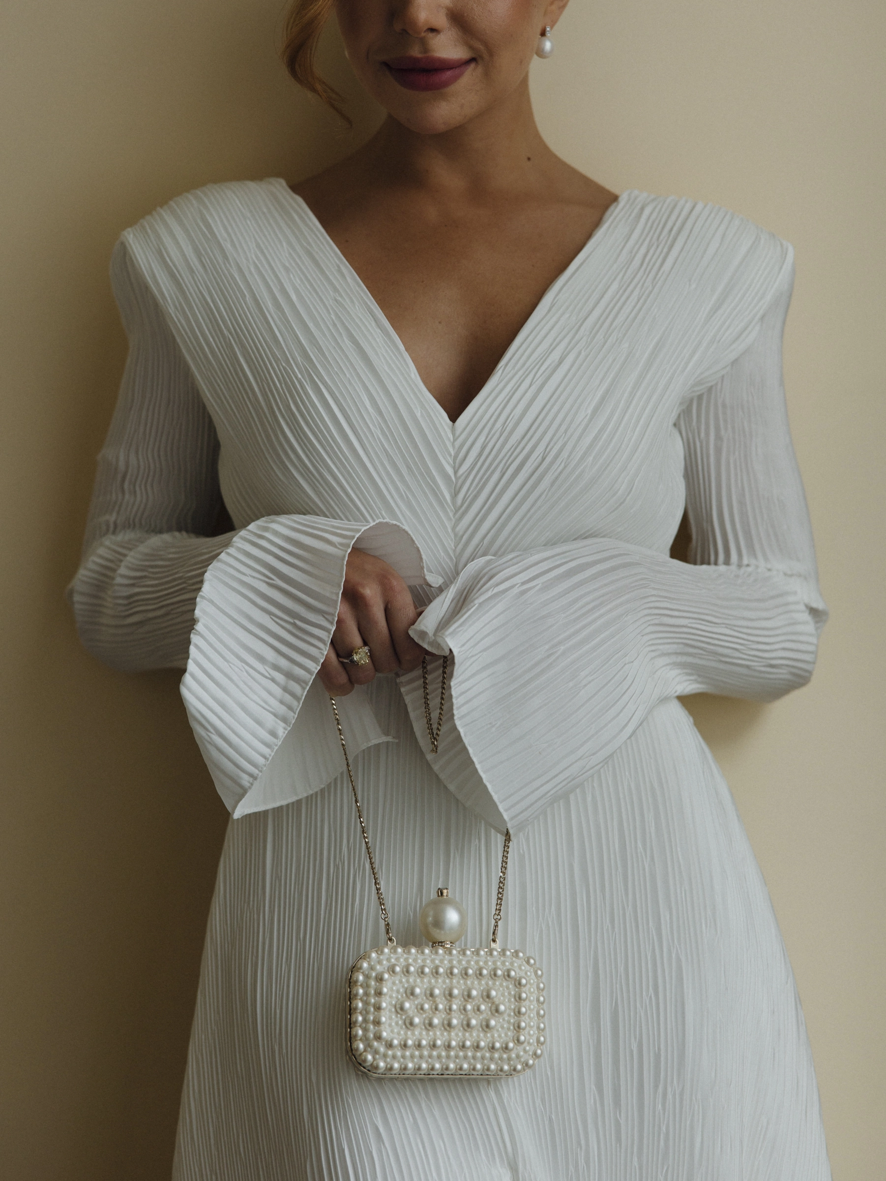 невеста в плиссированном платье держит жемчужную сумку-клатч