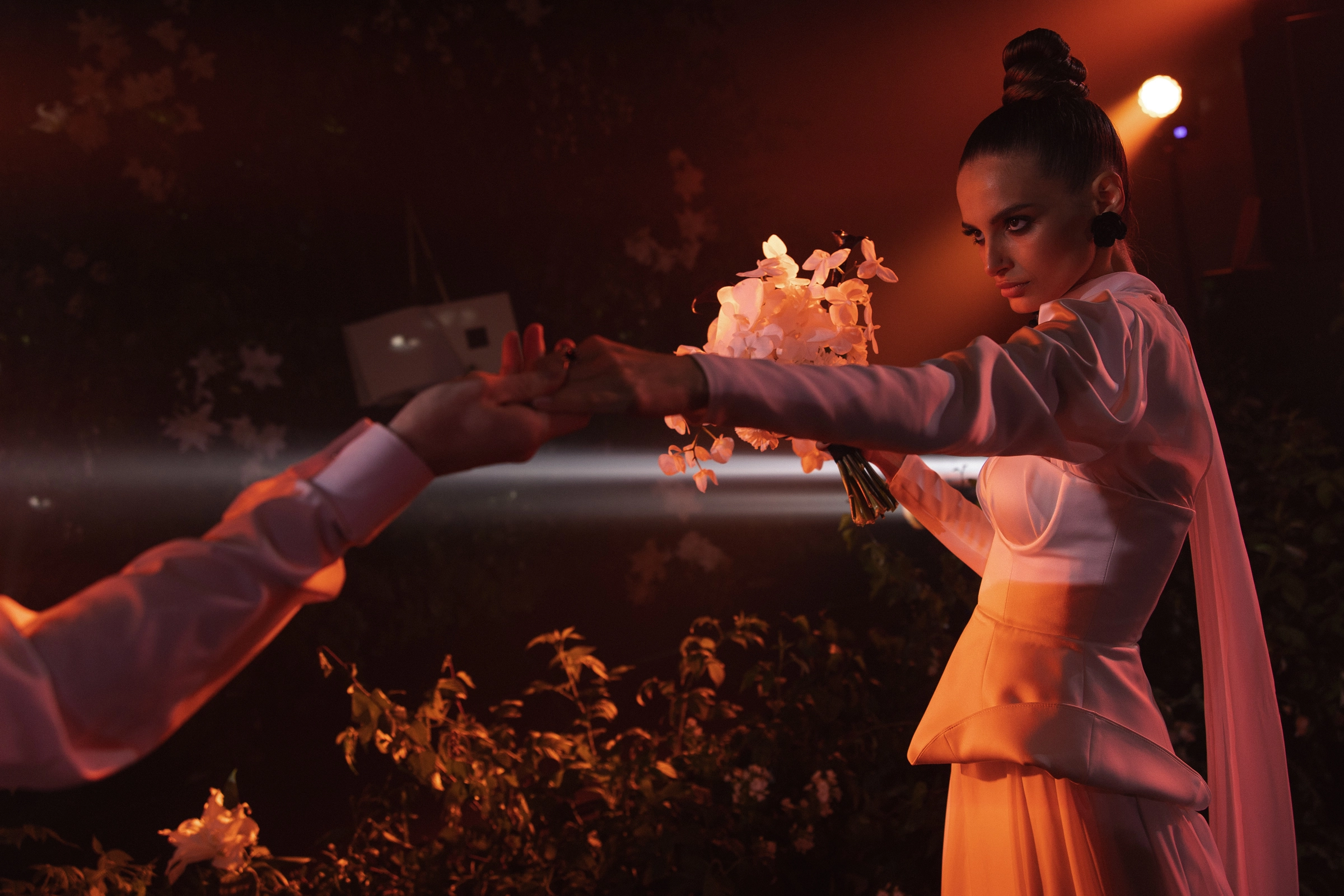 Рука тянется к цветам в тёплом оранжевом свете вечерней подсветки