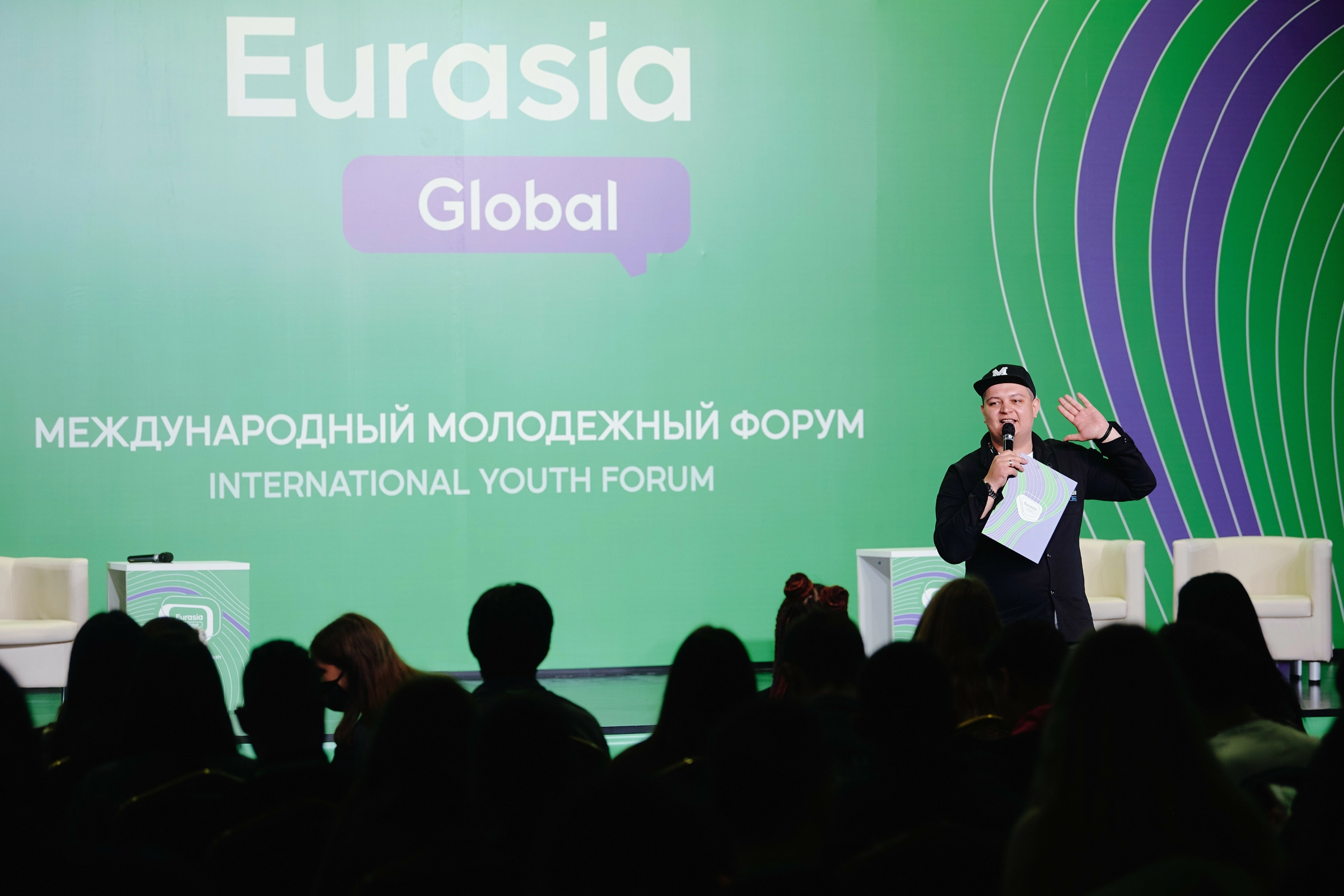 ведущий в берете выступает с микрофоном на сцене форума