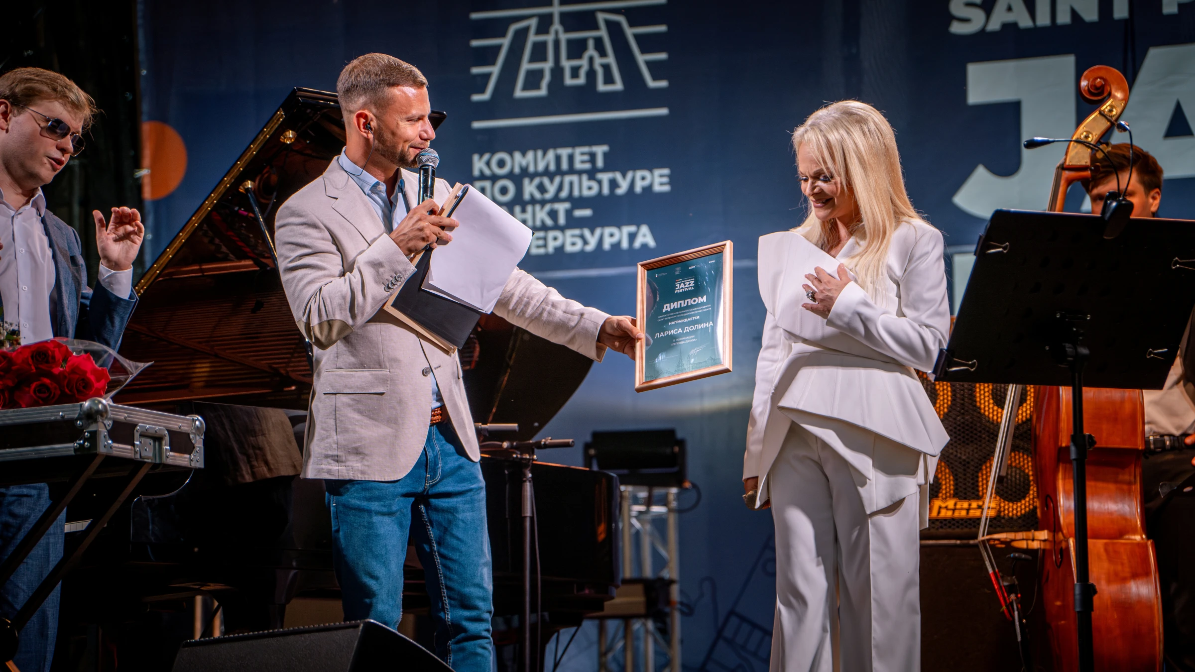 Женщина в белом костюме получает награду на сцене фестиваля