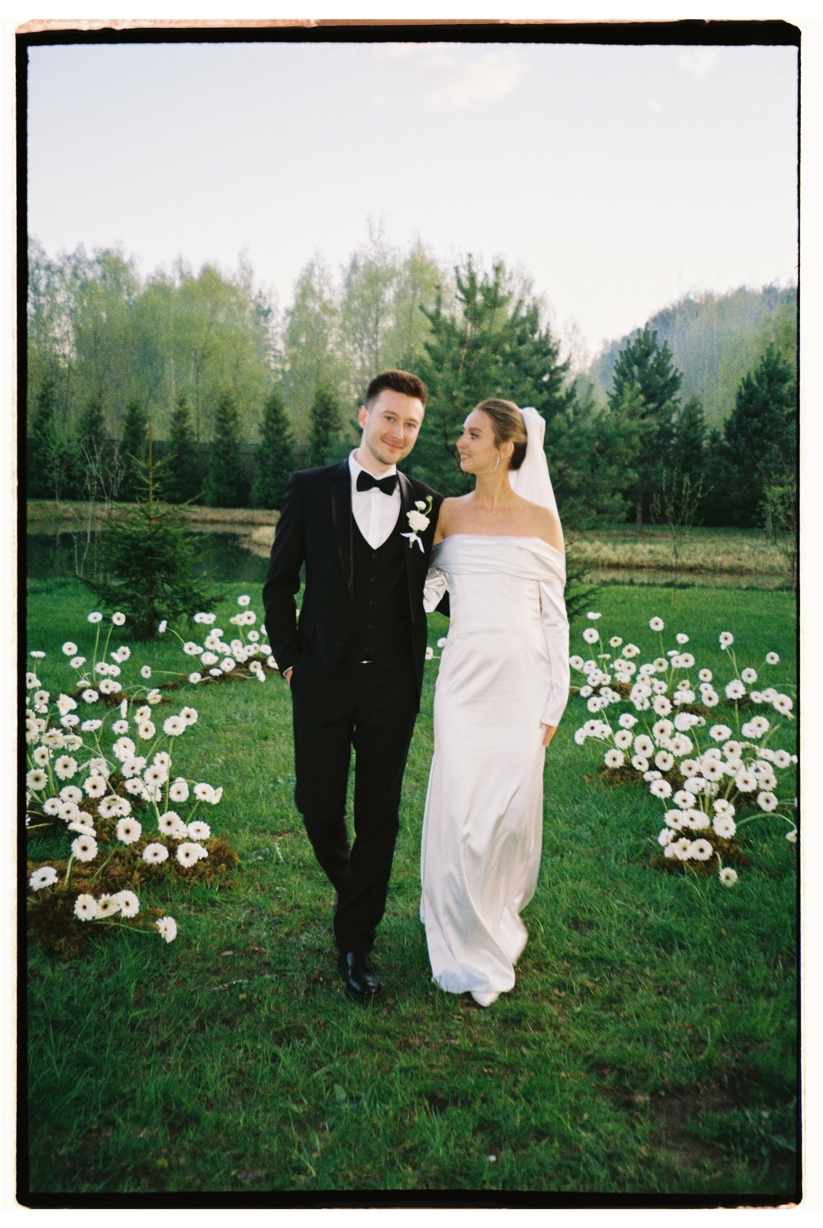 Молодожёны обнимаются на цветущем лугу среди белых ромашек летом