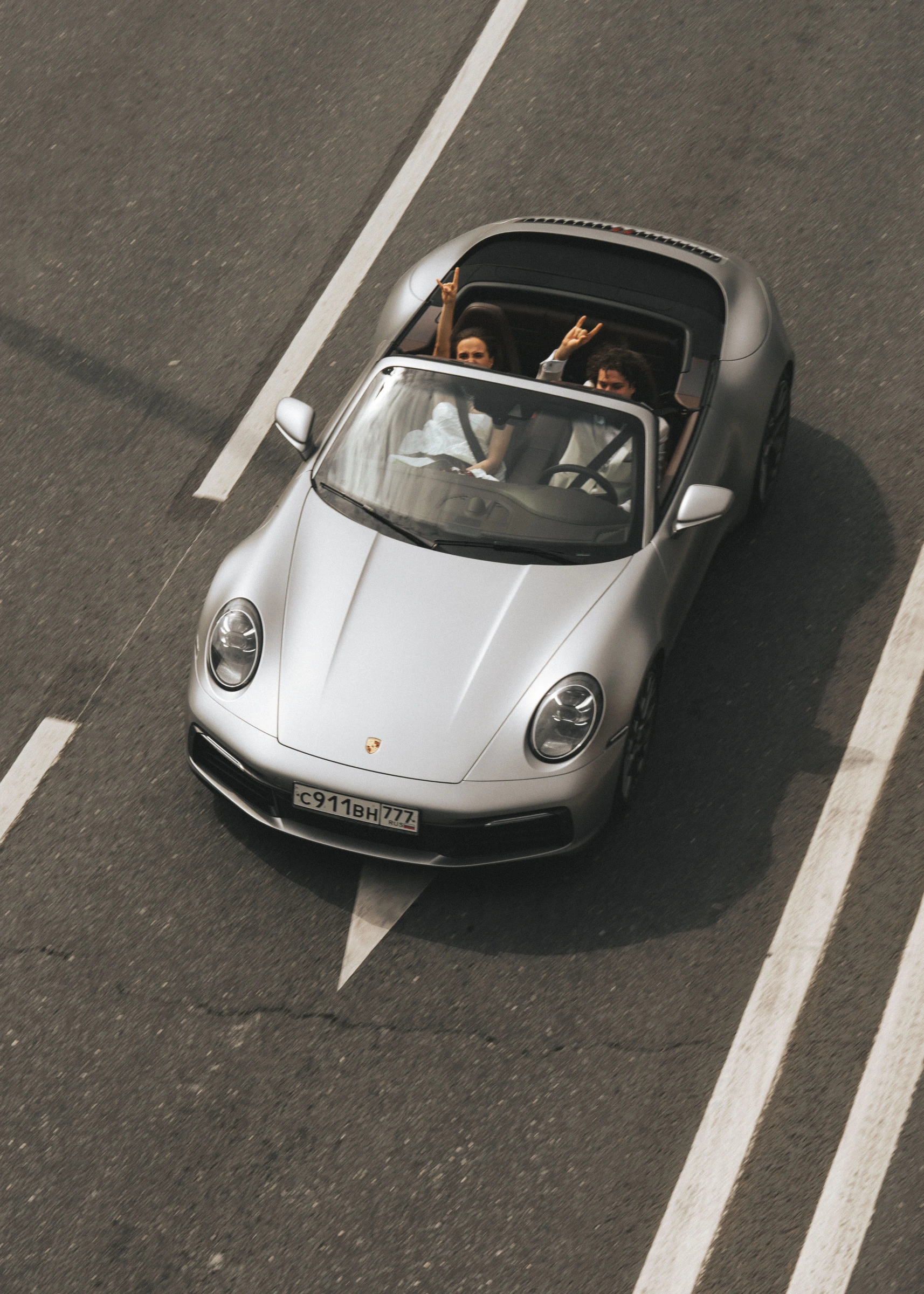 невеста и жених едут в серебристом кабриолете Porsche с откинутым верхом