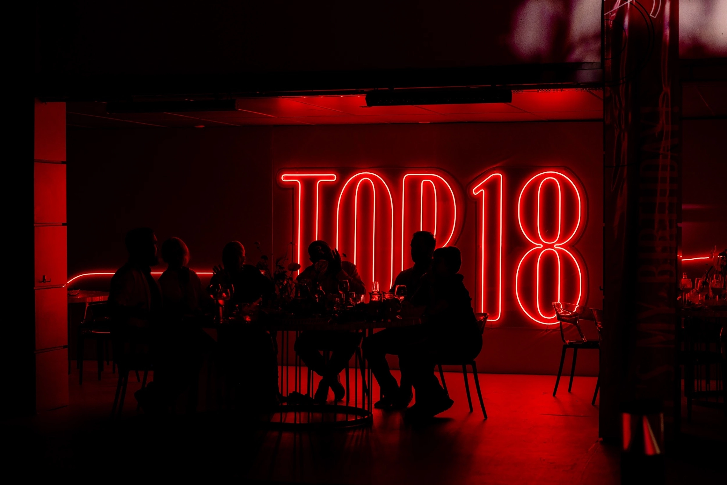 Тёмный зал с гостями на фоне светящейся надписи Top18