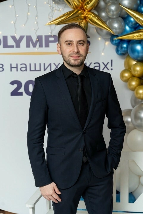 ведущий в тёмно-синем костюме на фоне праздничной фотозоны с золотыми шарами