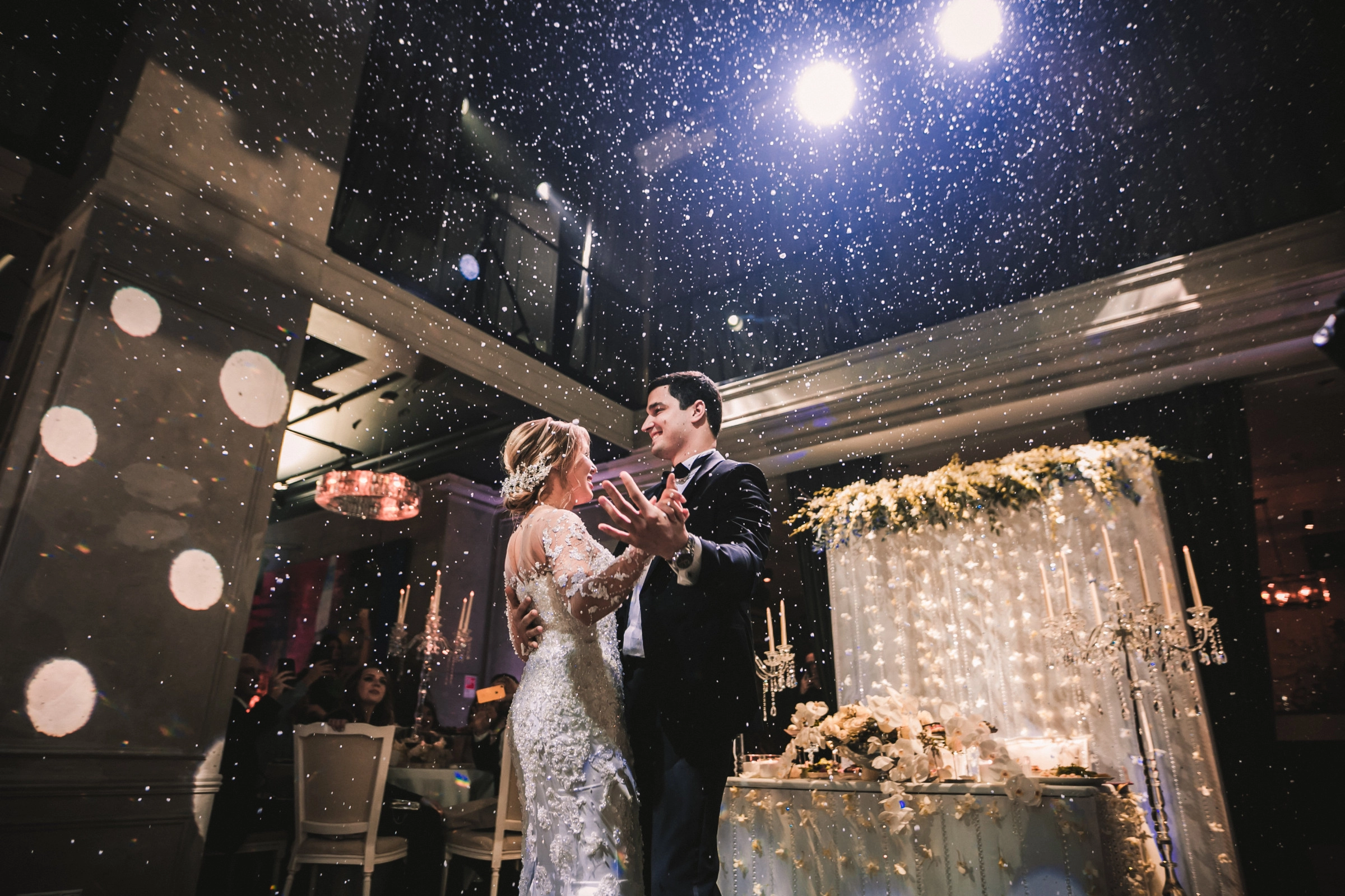 Портрет молодожёнов под потоком конфетти на фоне десертного стола