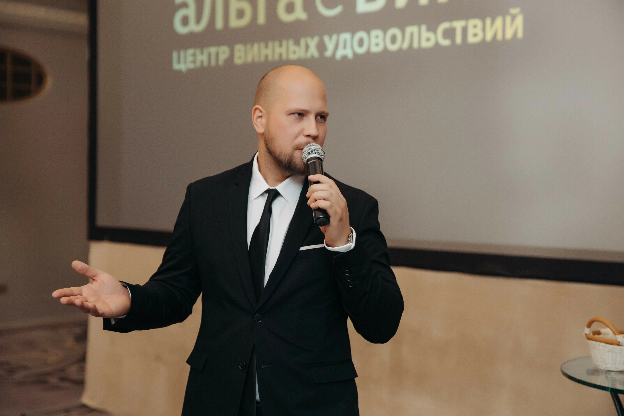 Ведущий в костюме жестикулирует у экрана с текстом