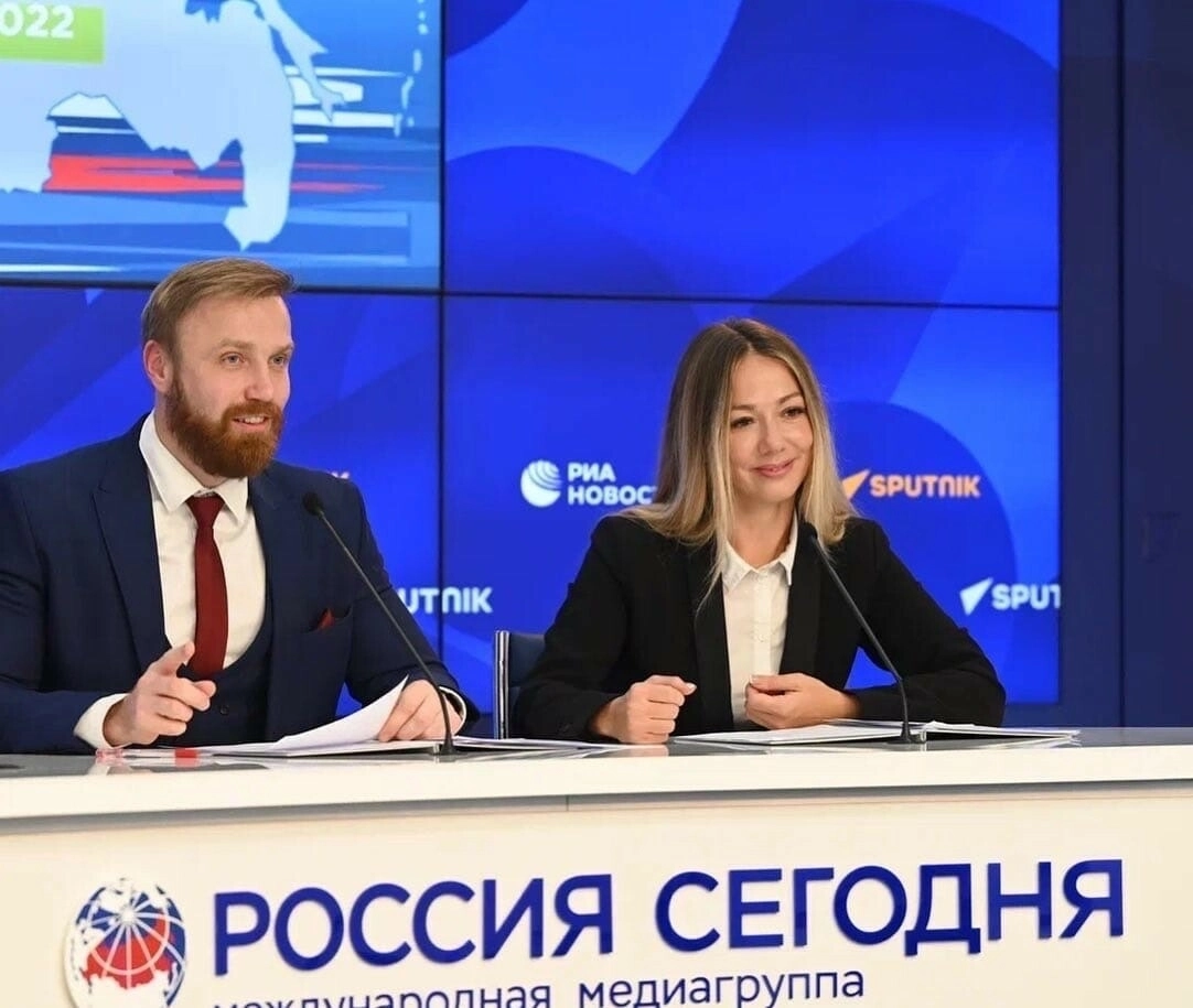 ведущие сидят за стойкой с микрофонами на пресс-конференции