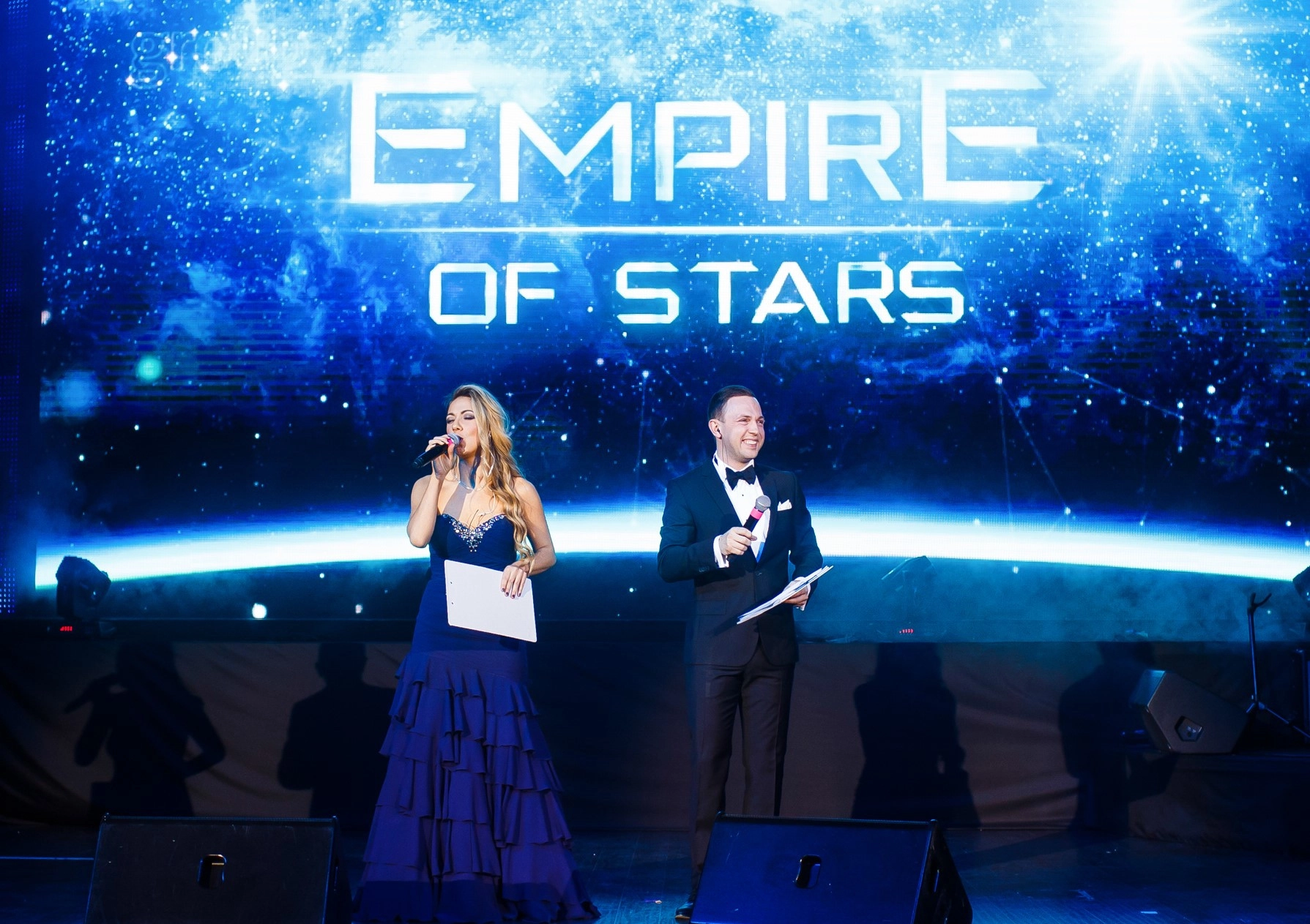 ведущие держат микрофоны на фоне надписи Empire of Stars